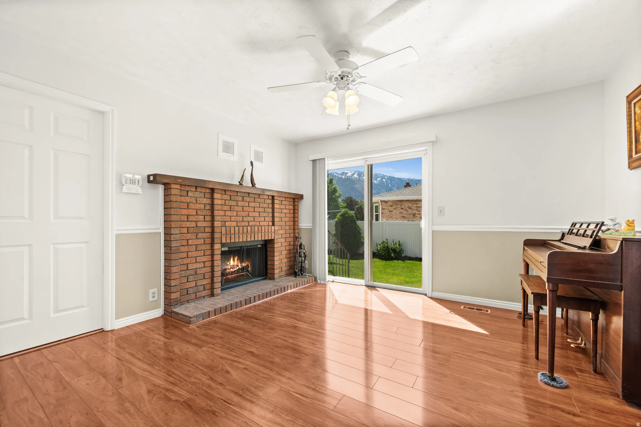 Living space featuring wood-finish flooring, a brick fireplace with a wood mantel, and a ceiling fan