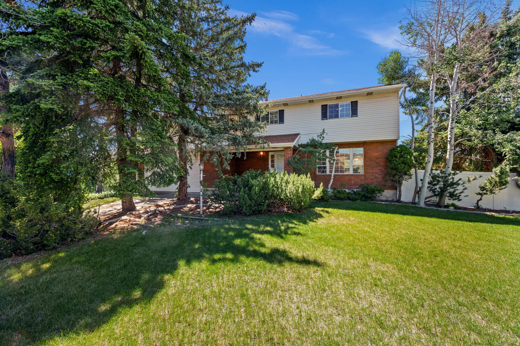 Two-story residence featuring a brick and siding exterior, front lawn, and mature trees