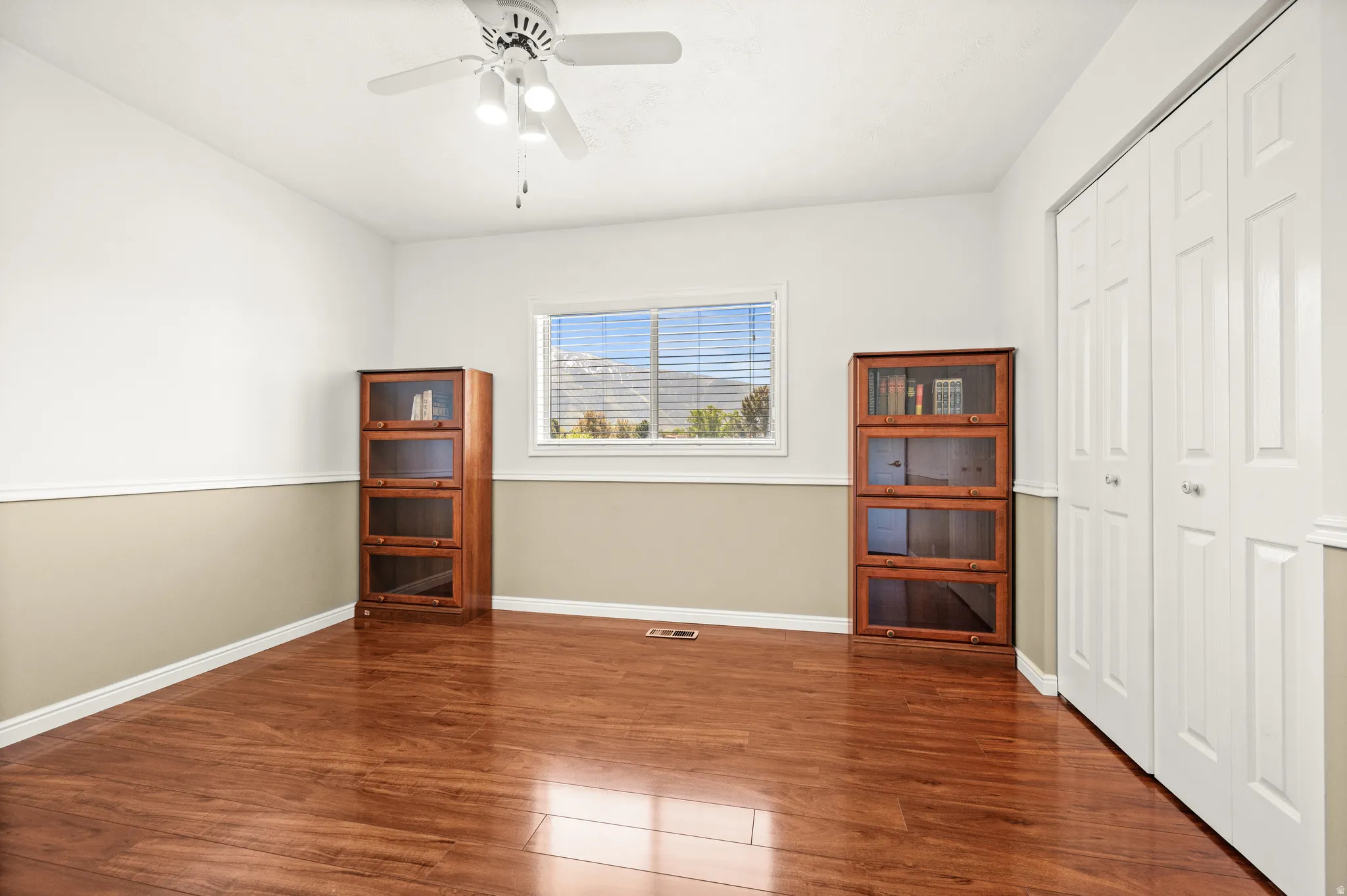 Room featuring wood-finish flooring, white bifold closet doors, a ceiling fan with integrated lighting, and a window with blinds