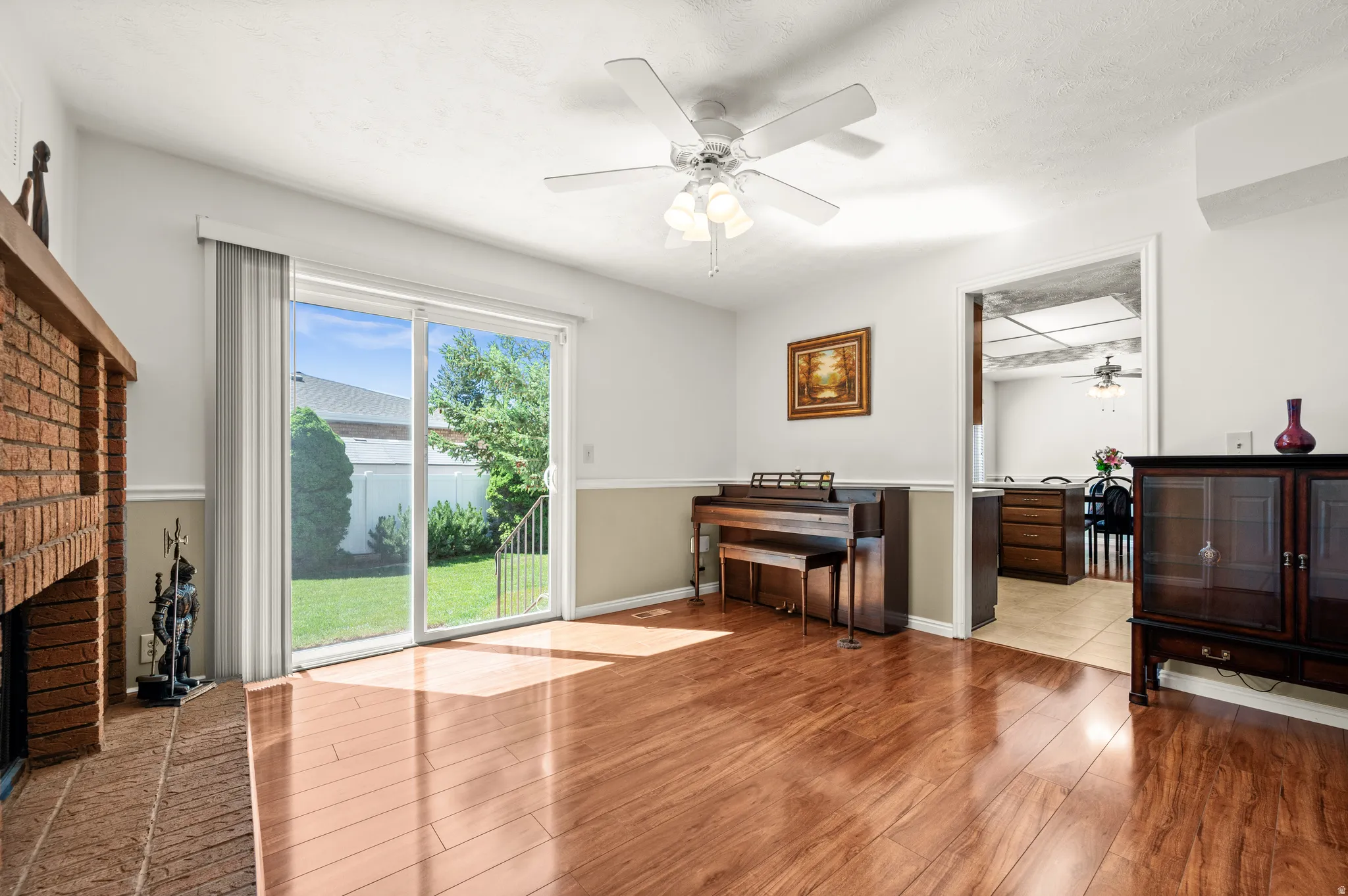 Living area featuring wood-finish flooring, a brick fireplace, a ceiling fan, and sliding glass doors opening to a grassy outdoor space