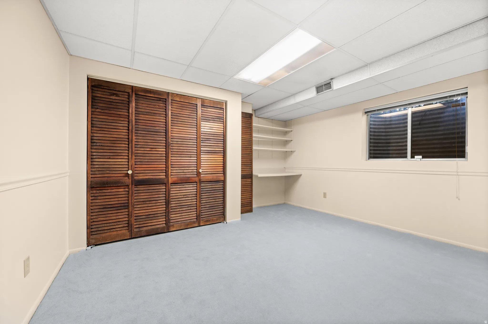 Spacious room featuring light blue carpeting, cream-painted walls, and a dropped ceiling with integrated lighting