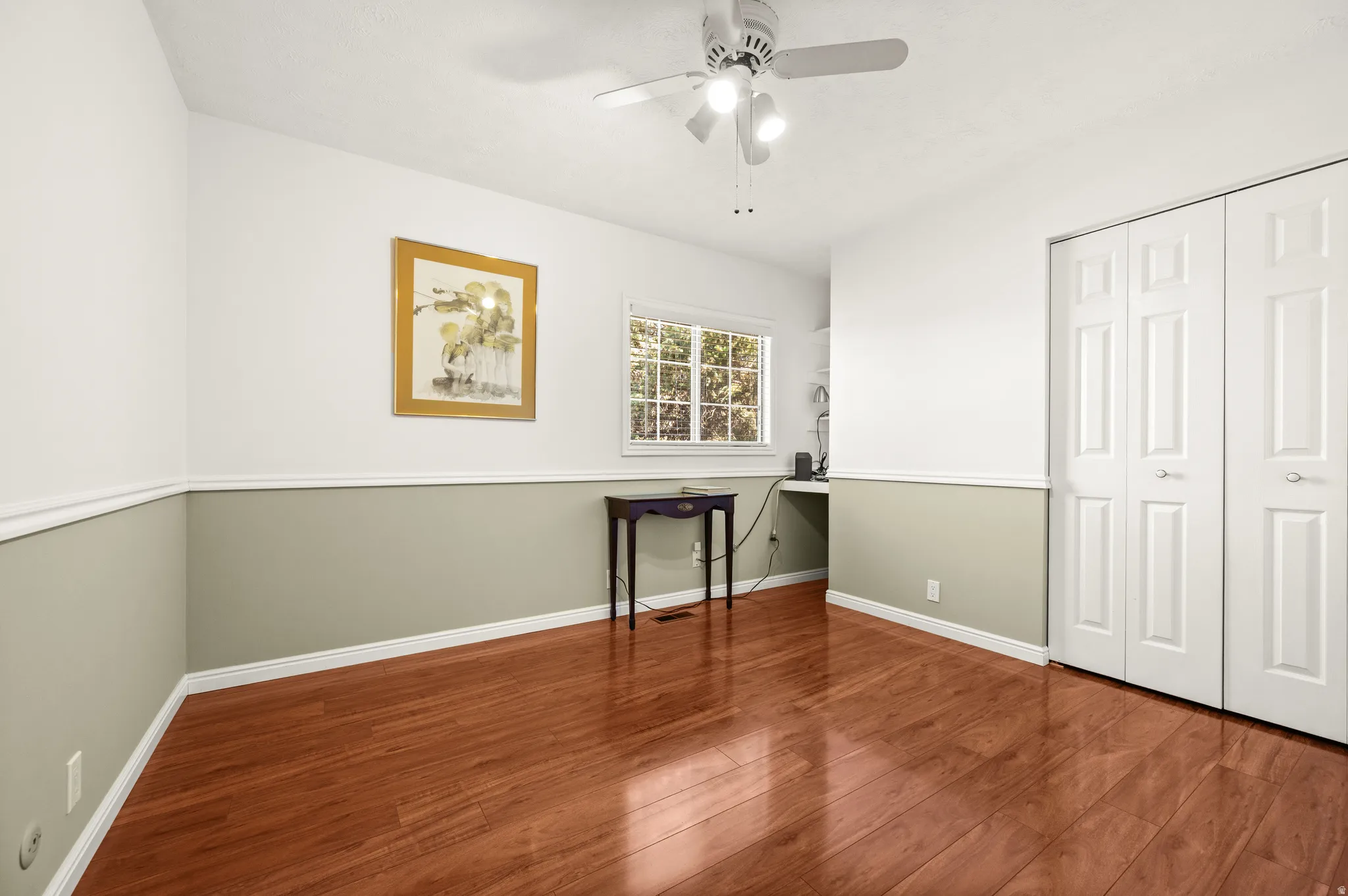 Room featuring rich wood-finish flooring, a ceiling fan with integrated lighting, and dual bifold closet doors