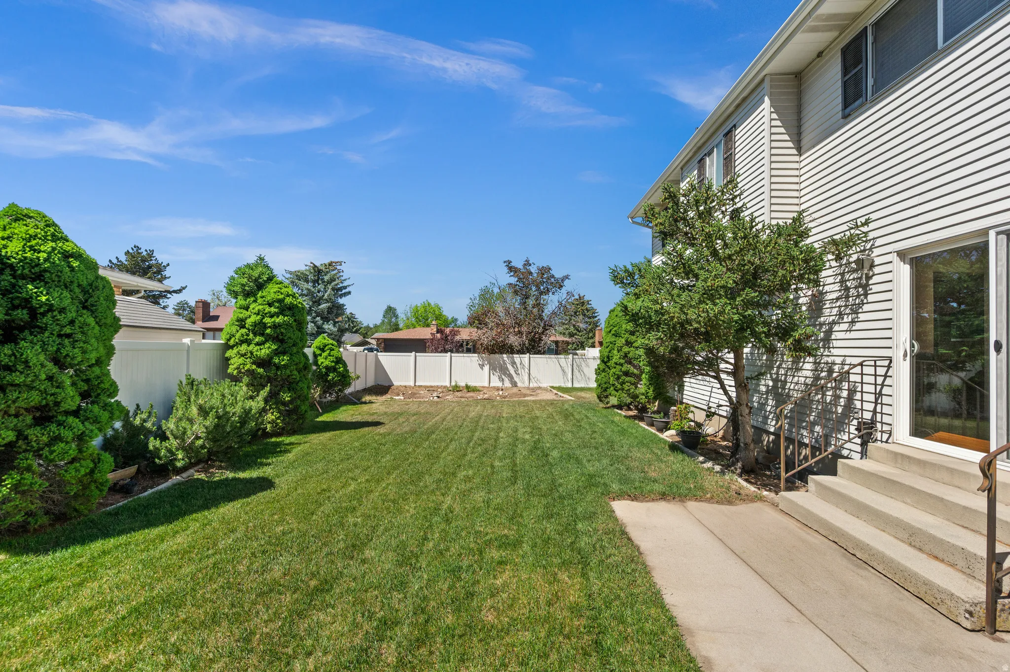 Expansive grassy yard area with a white privacy fence