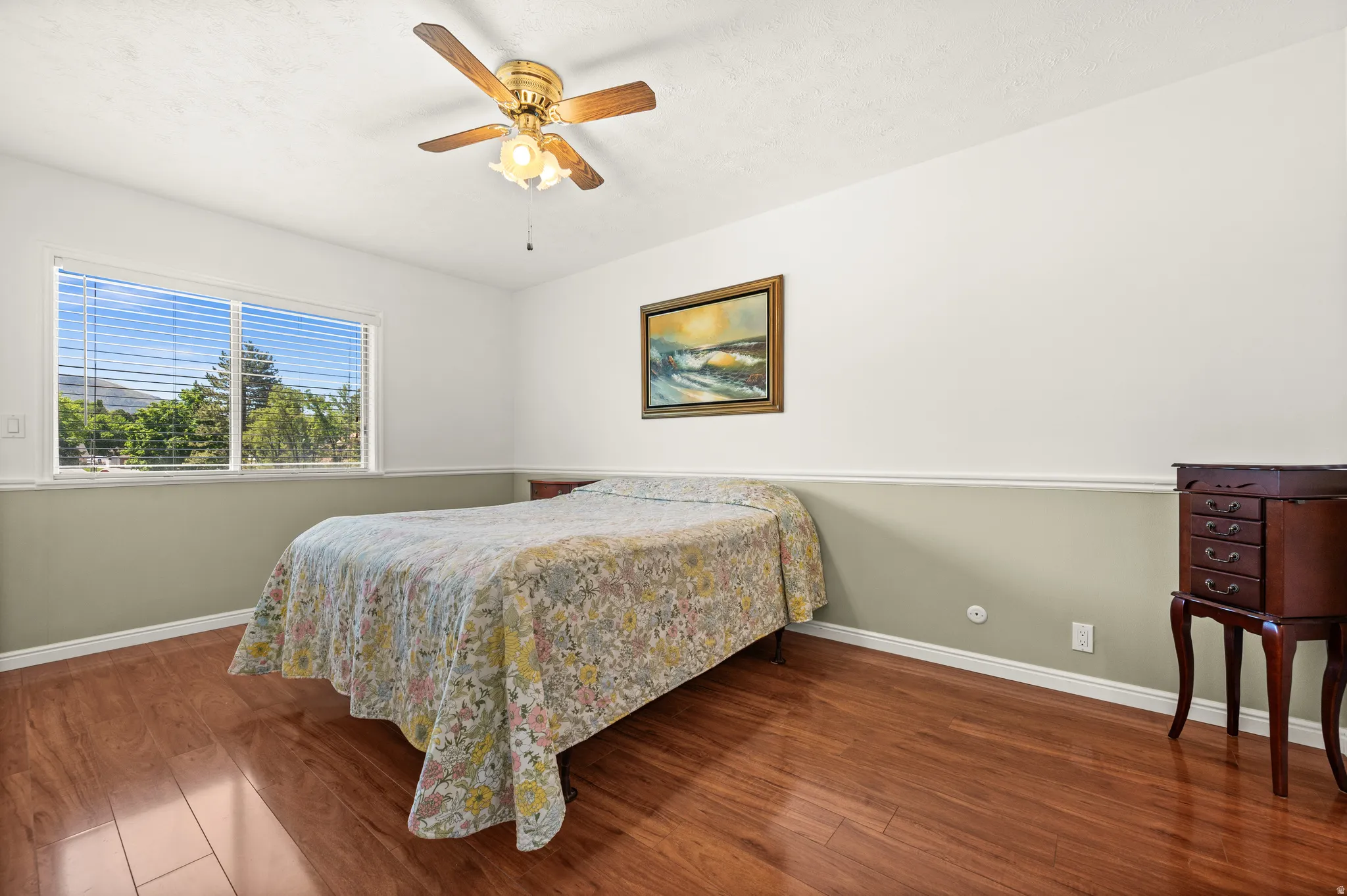 Spacious room featuring wood-finish flooring, a large window, and a ceiling fan with integrated lighting