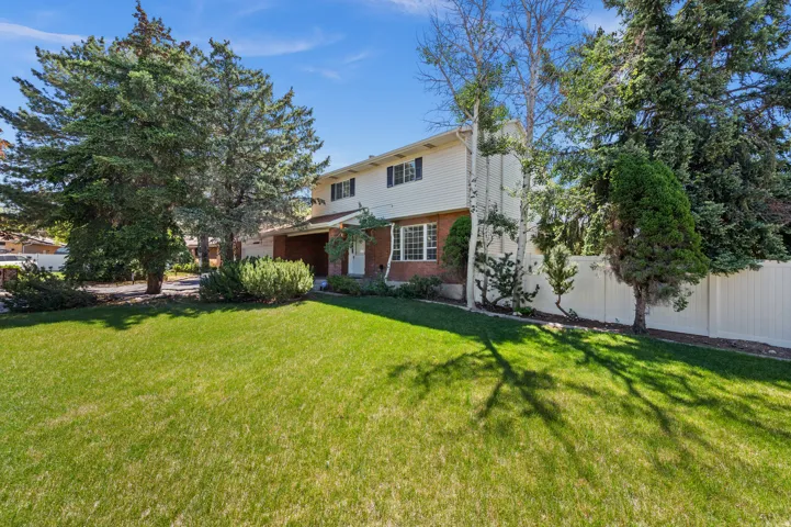 Two-story residence featuring a brick and white siding exterior, a manicured lawn, mature evergreen trees, and a white privacy fence