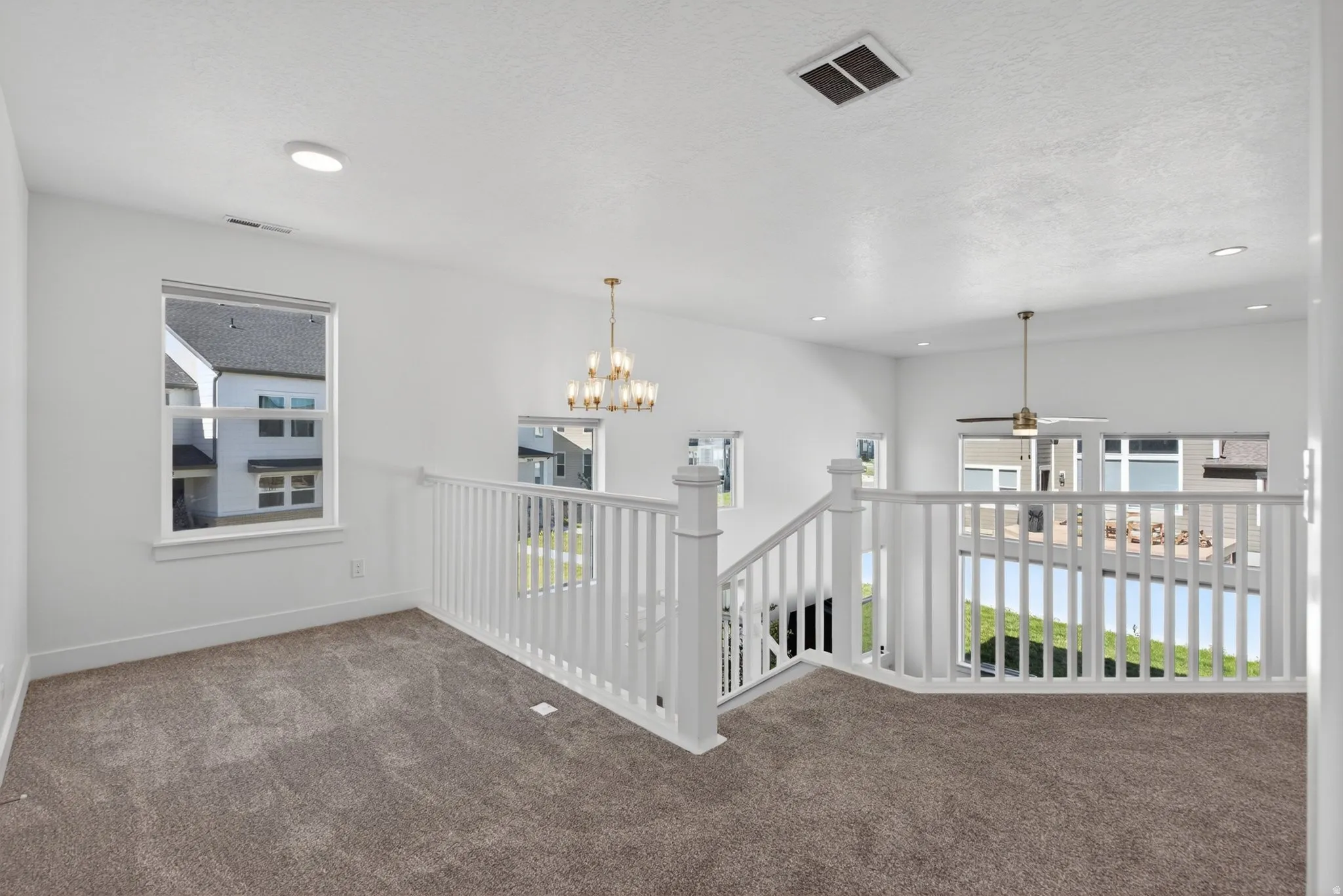 Big open loft area with neutral carpeting, white banister railing, and recessed lighting. Large