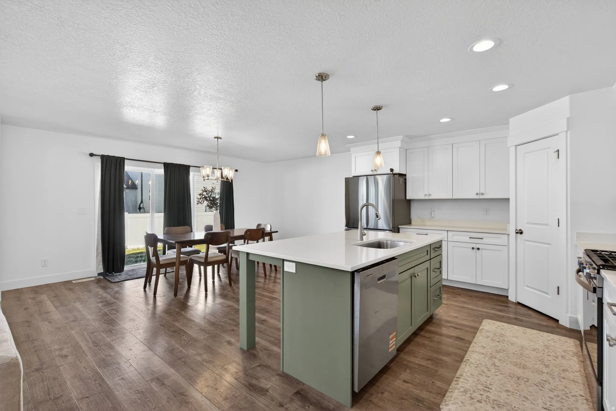 Open-concept living space featuring wood-finish flooring, a kitchen island with a built-in sink and dishwasher, white cabinetry, stainless steel appliances, and pendant lighting with walk out to backyard