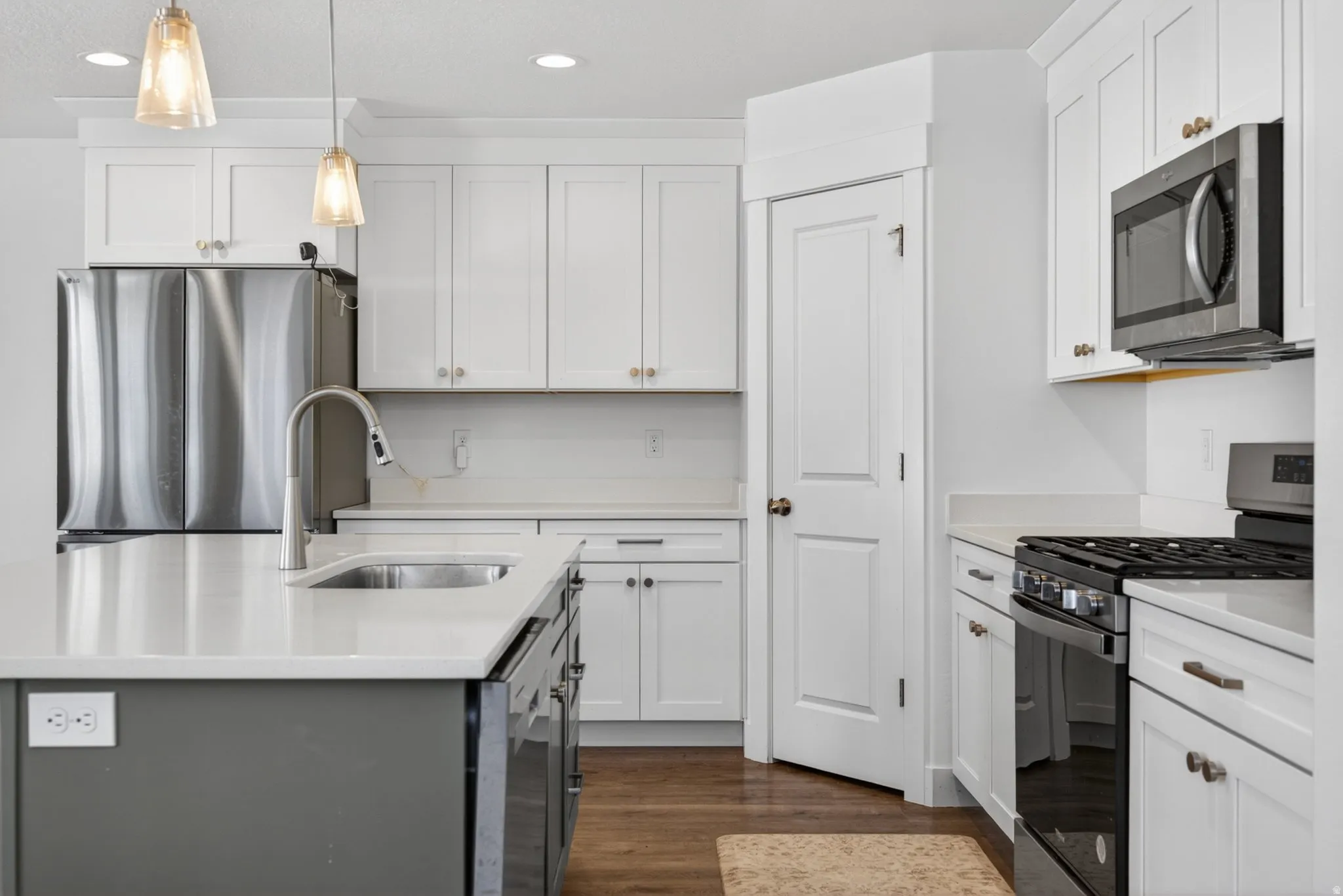 Modern kitchen featuring white shaker cabinetry, stainless steel appliances, a center island with sink and pendant lighting, and lvp  flooring