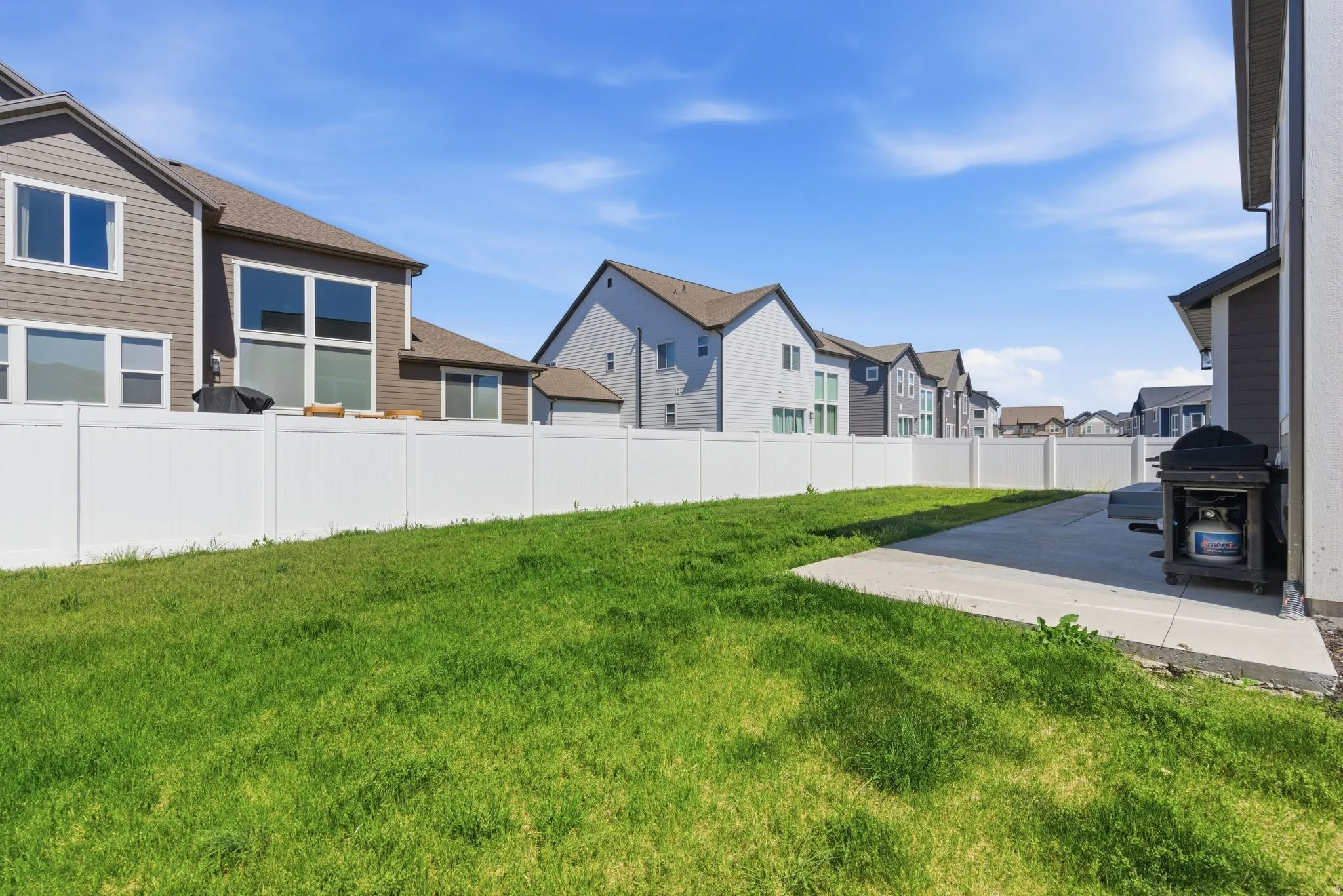 Expansive backyard featuring a white vinyl privacy fence, a concrete patio, and a grass lawn