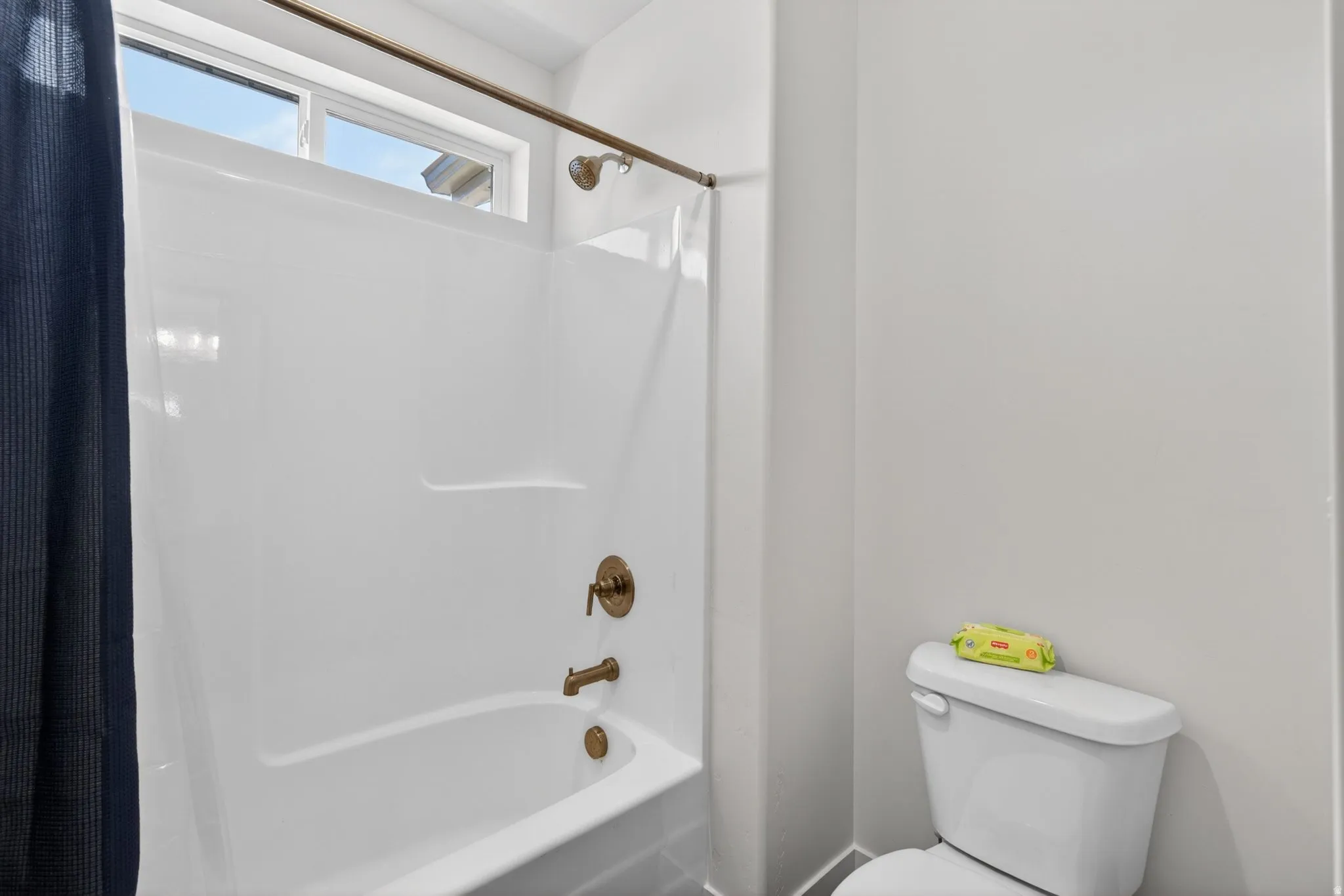 White shower-over-tub unit with bronze-finish fixtures and an upper transom window