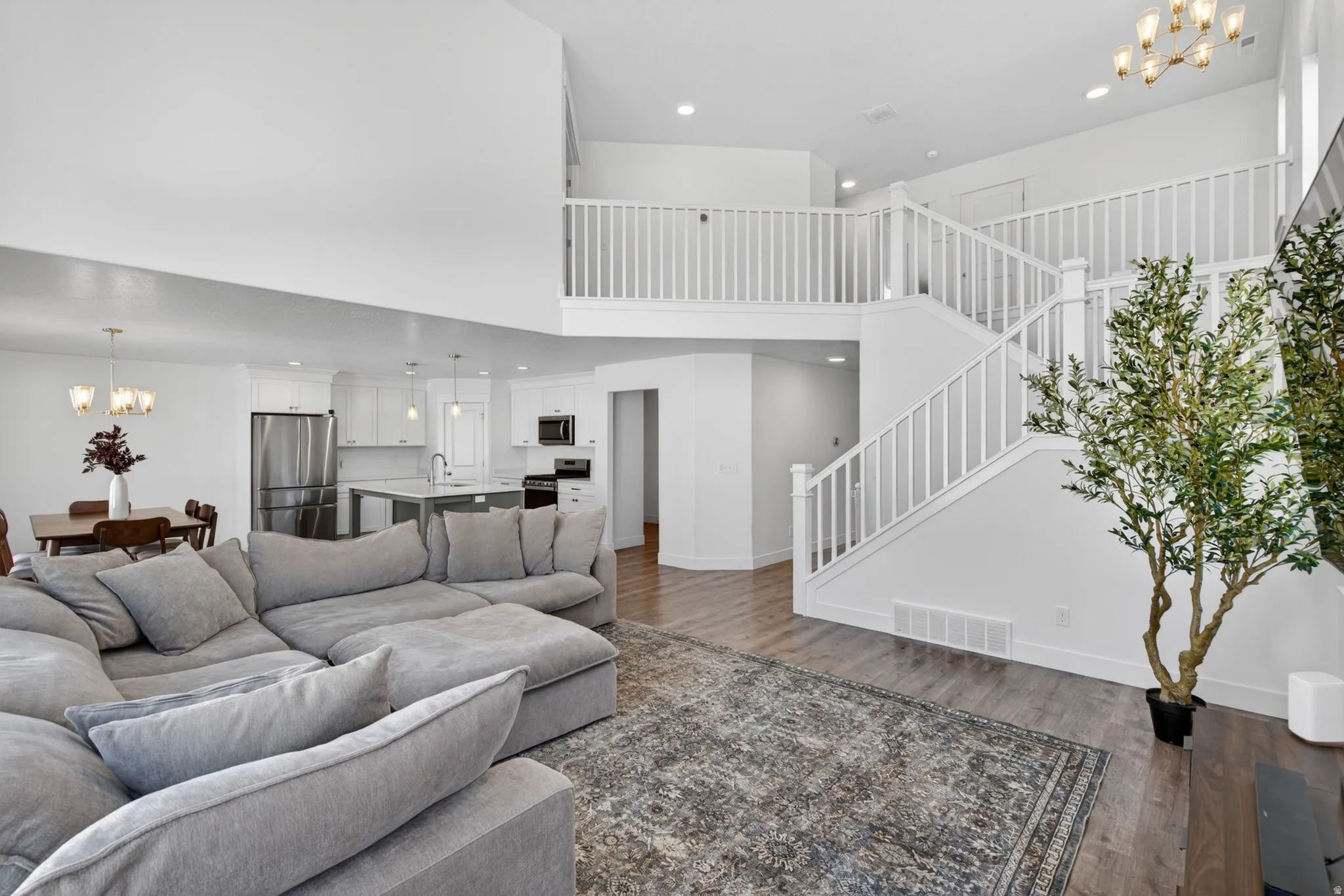 Spacious open-concept living area featuring high vaulted ceilings, lvp flooring, staircase and view of kitchen and dining room.