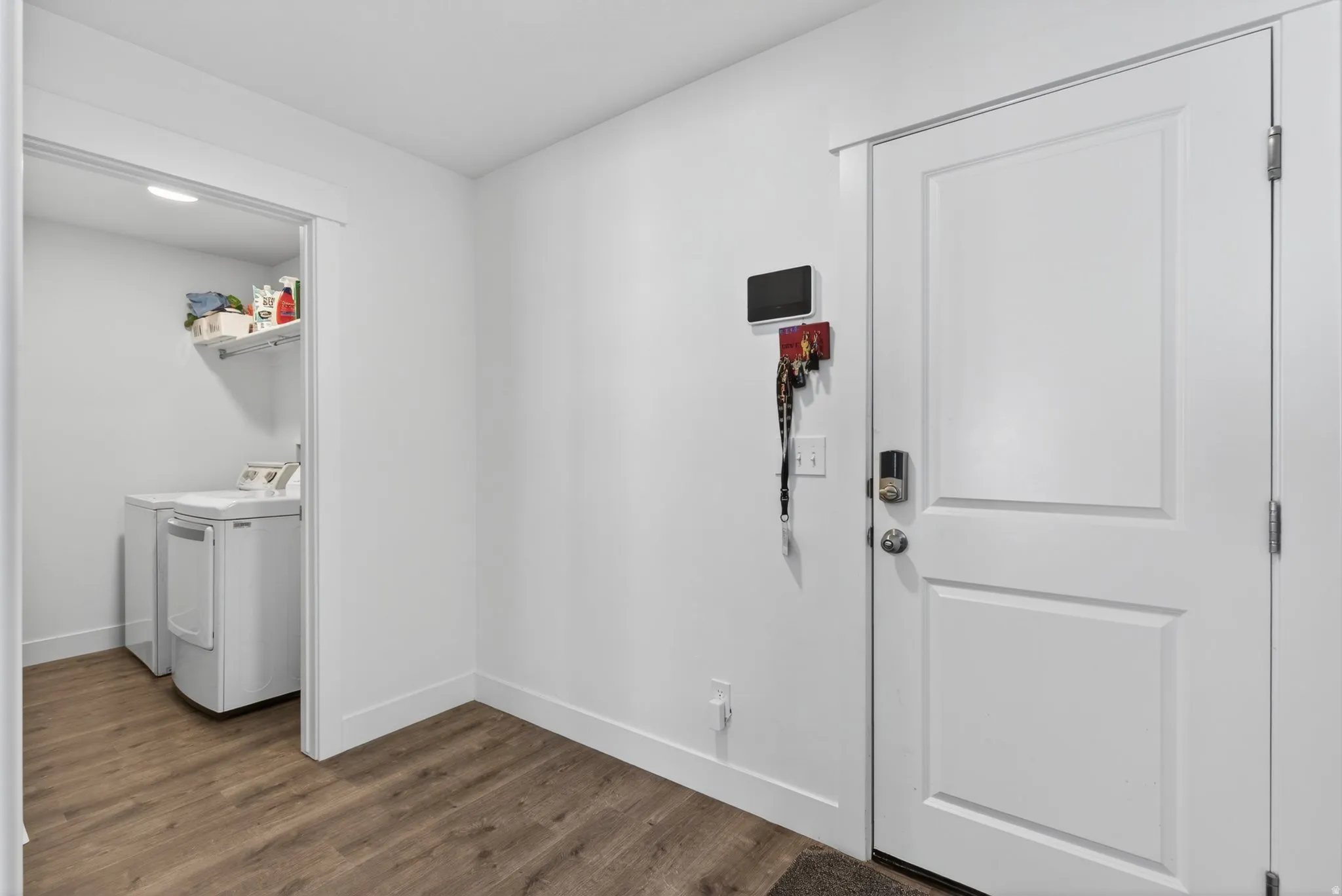 Dedicated laundry area featuring a white floating shelf, white baseboards, and wood-finish flooring