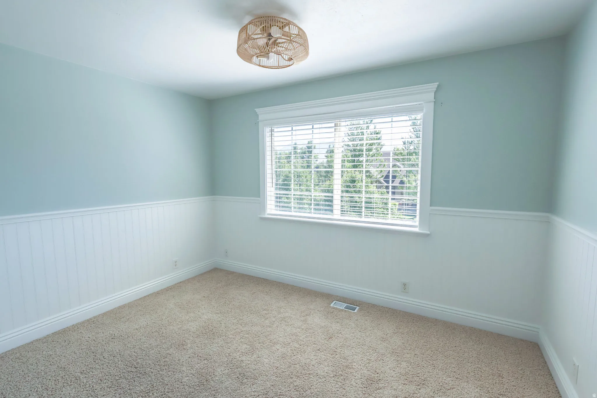 Light-filled room featuring a broad window with blinds, wainscoting, and carpet flooring