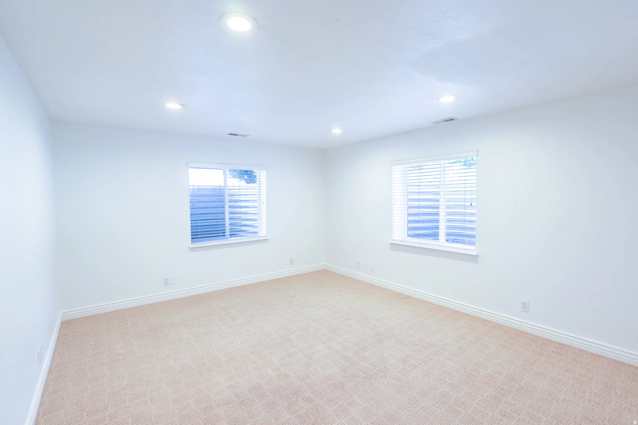 Bright room featuring two windows with horizontal blinds, recessed lighting, and neutral-toned carpet