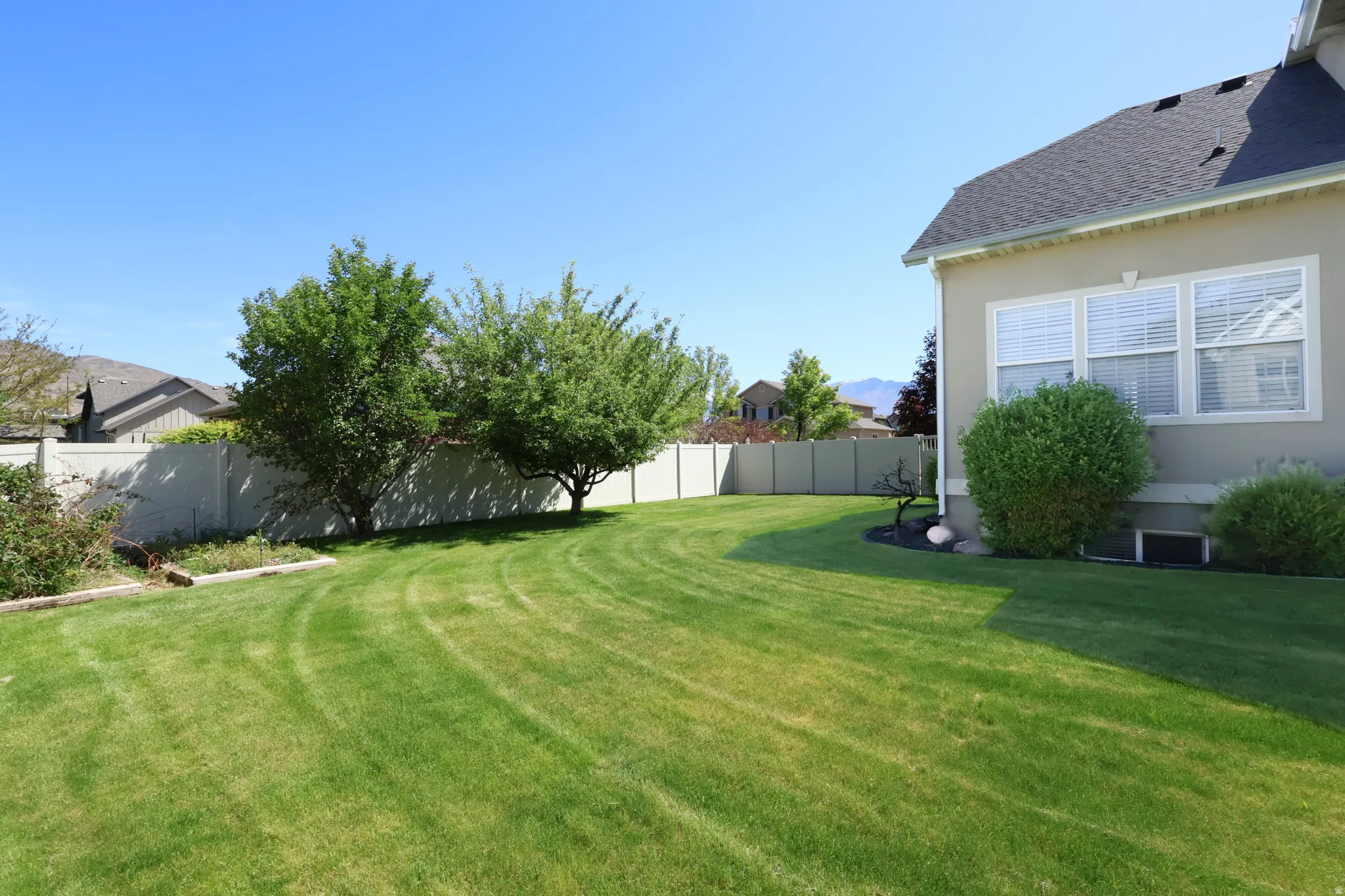 Expansive green lawn with a perimeter fence, mature trees, and a stucco exterior
