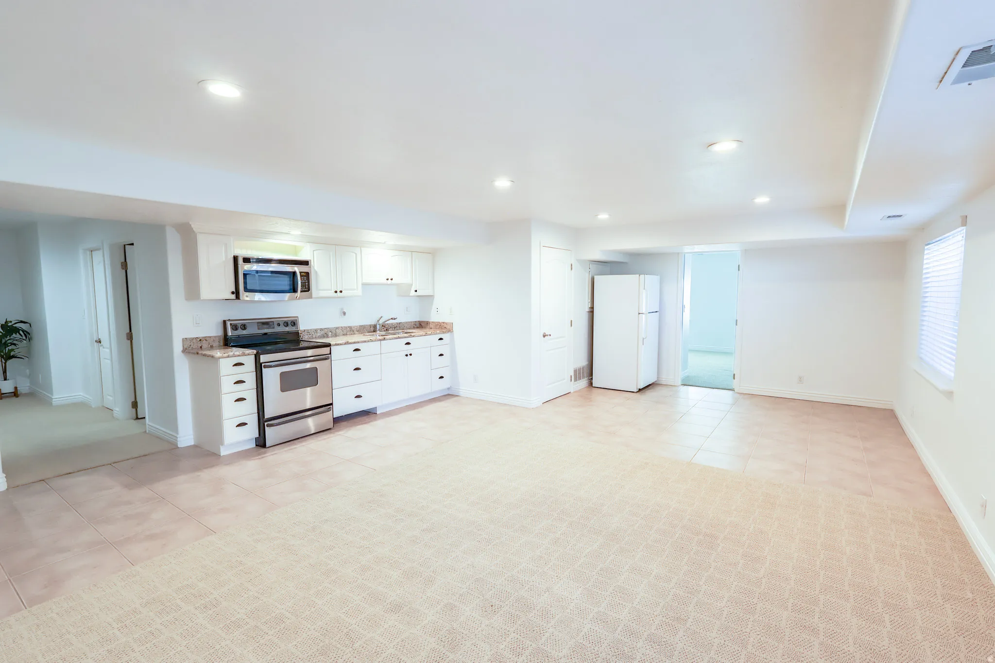 Open-concept living area featuring a full kitchen with white cabinetry, stainless steel appliances, and stone countertops
