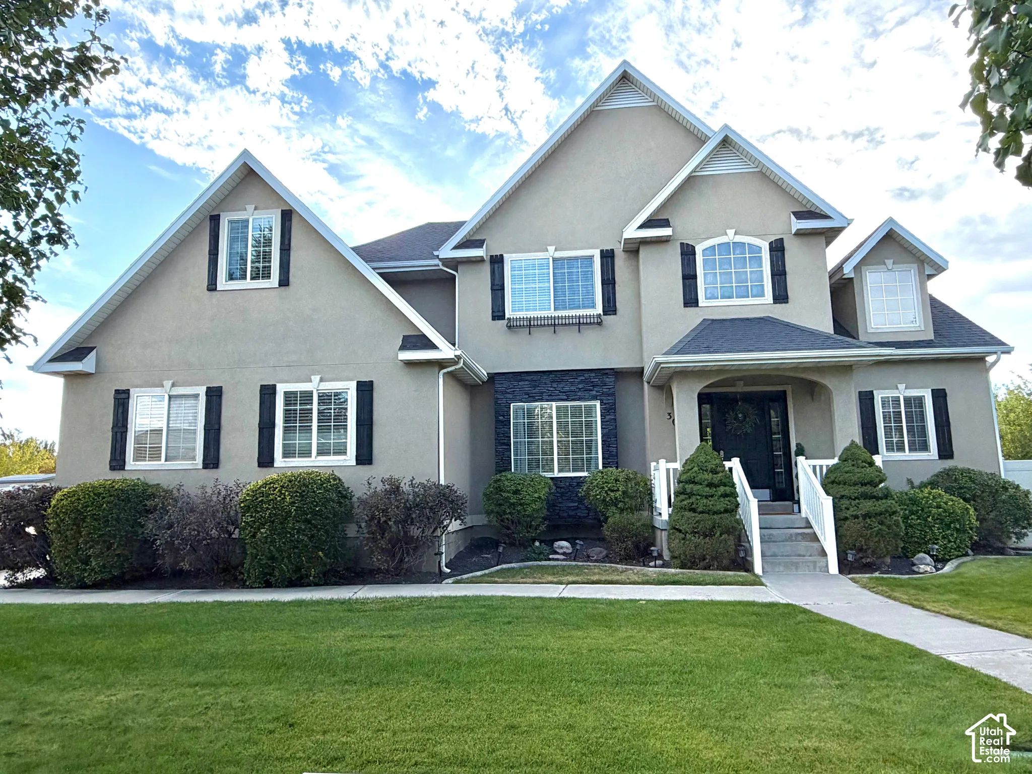 Stucco exterior with stone accents, multiple gables, covered entry, and a paved walkway
