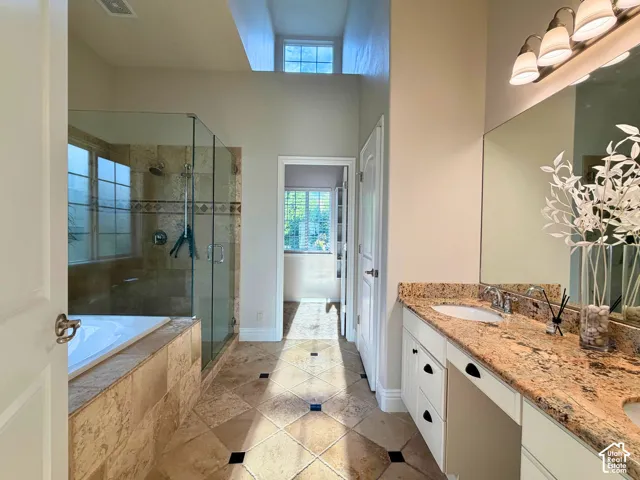 Dual vanity with stone countertop and integrated sinks, glass-enclosed shower with tile surround, soaking tub with tile surround, and tile flooring