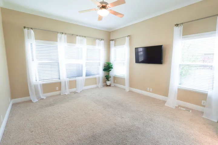 Spacious room featuring neutral carpeting, extensive window treatments, and a ceiling fan
