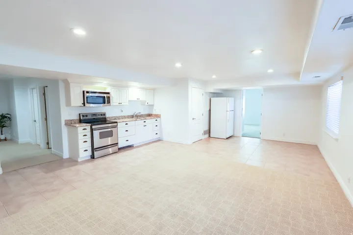 Open-concept living area featuring a full kitchen with white cabinetry, stainless steel appliances, and stone countertops