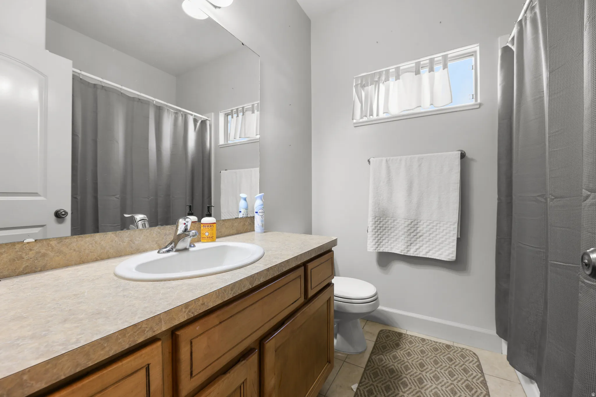 Bathroom featuring a laminate countertop vanity with an integrated sink, wood-finish cabinetry, full-width mirror, and a horizontal window