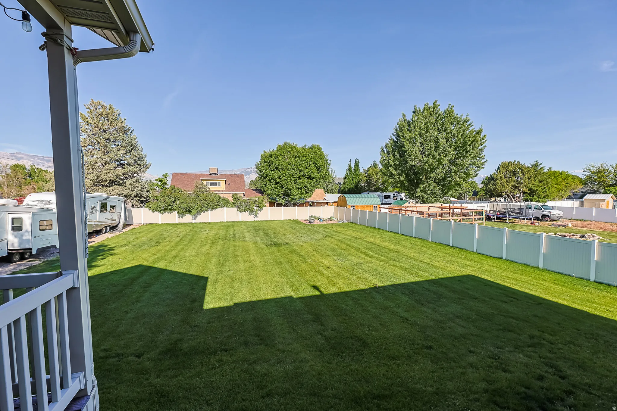 Expansive backyard featuring a manicured lawn, a full white privacy fence, and a partially visible porch with white railings