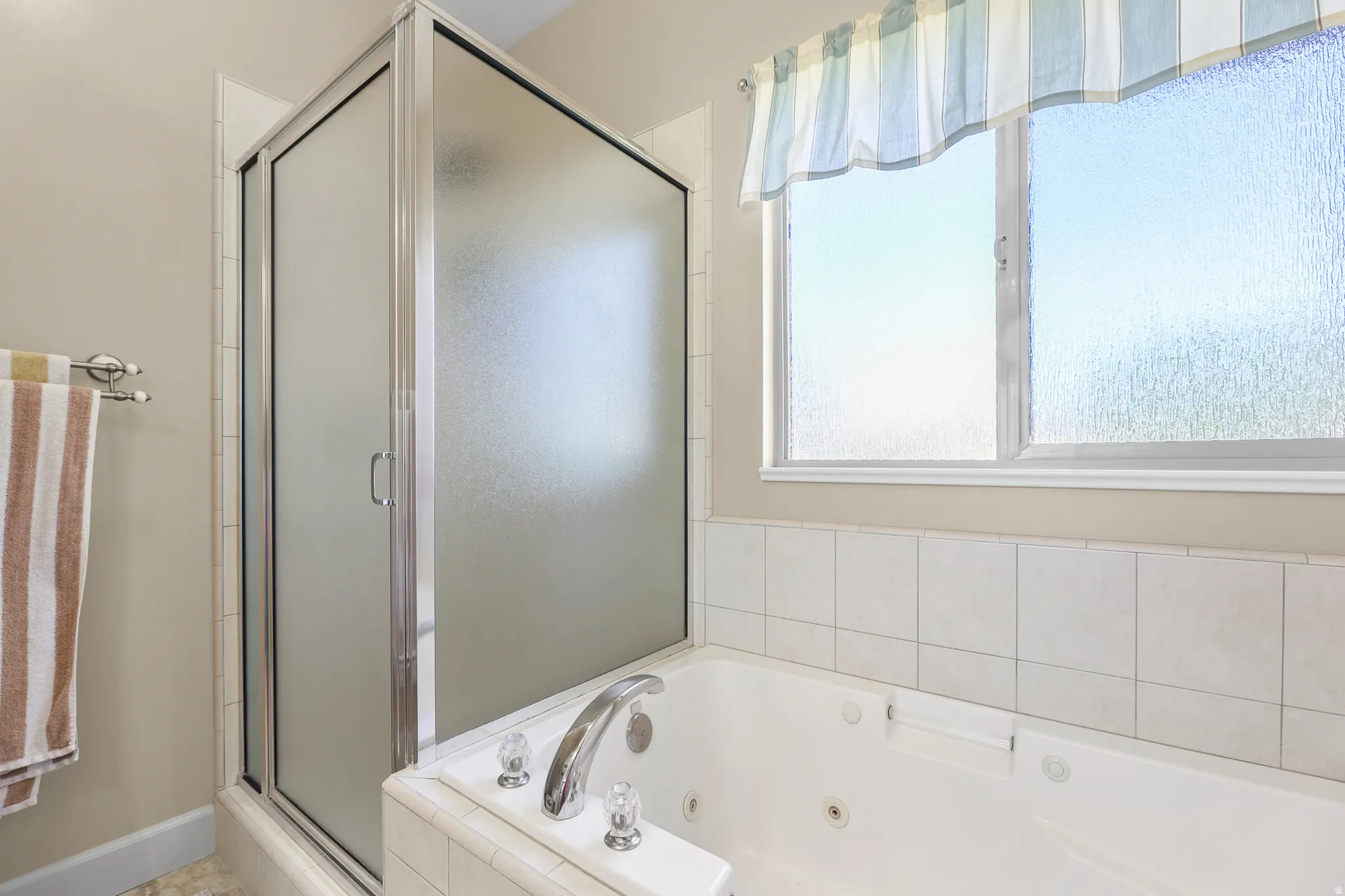 Enclosed shower with frosted glass panels, built-in jetted tub, ceramic tile surround, and a double-pane window