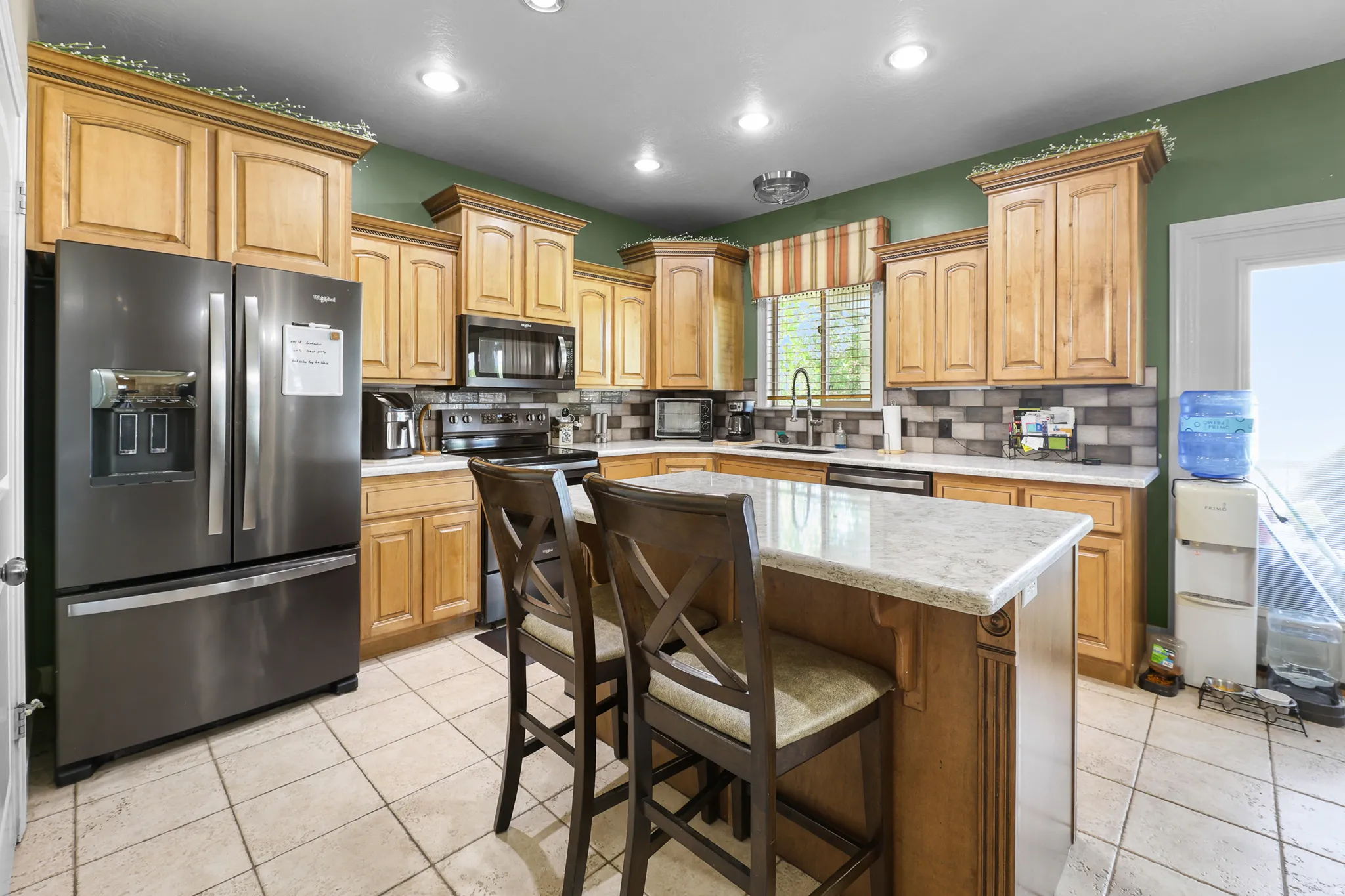 Kitchen featuring a central island with countertop seating, light wood cabinetry, stone-look countertops, tiled backsplash, and recessed lighting