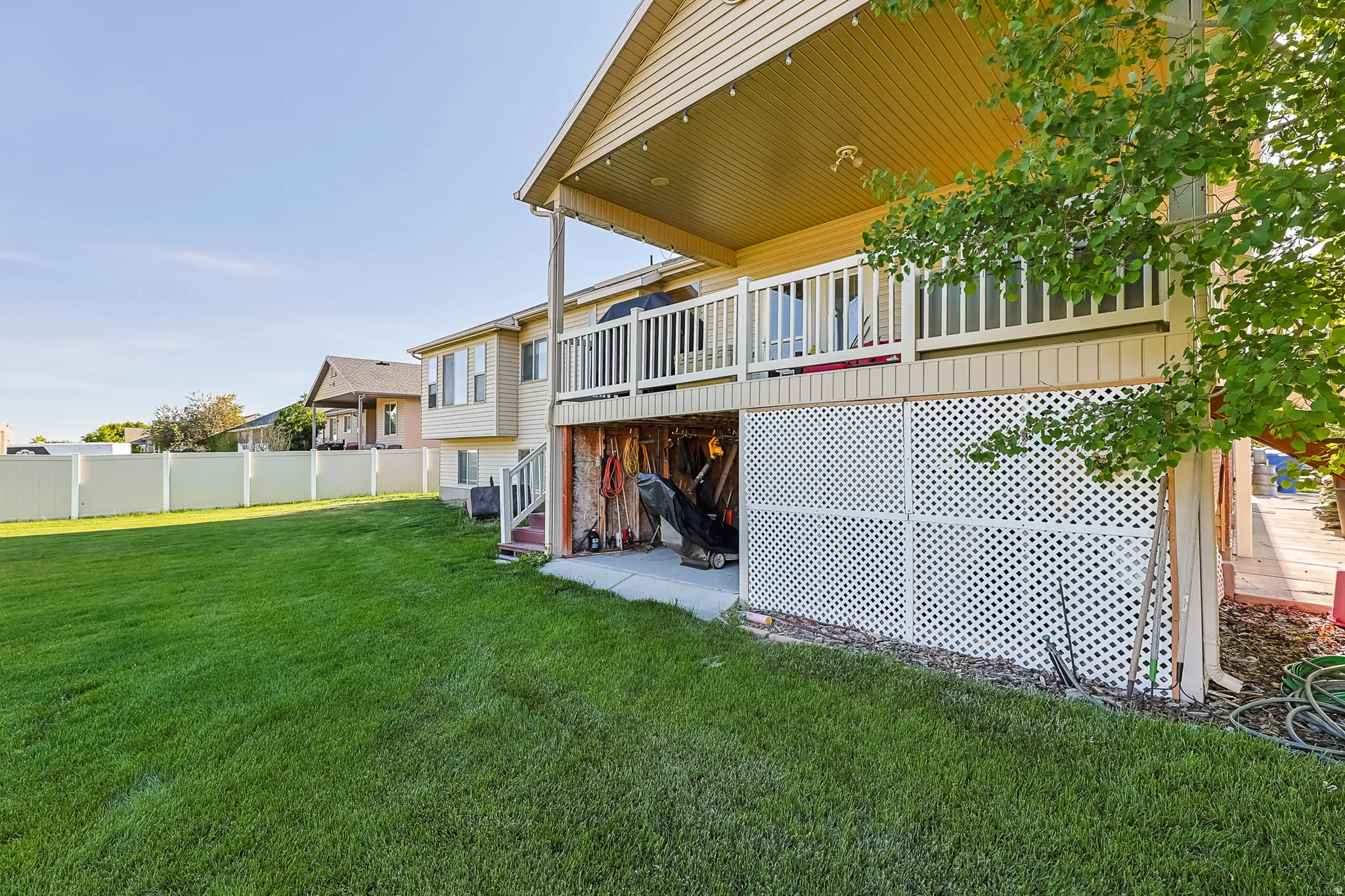 Expansive green lawn featuring a covered patio, upper-level deck, white lattice skirting, and a privacy fence