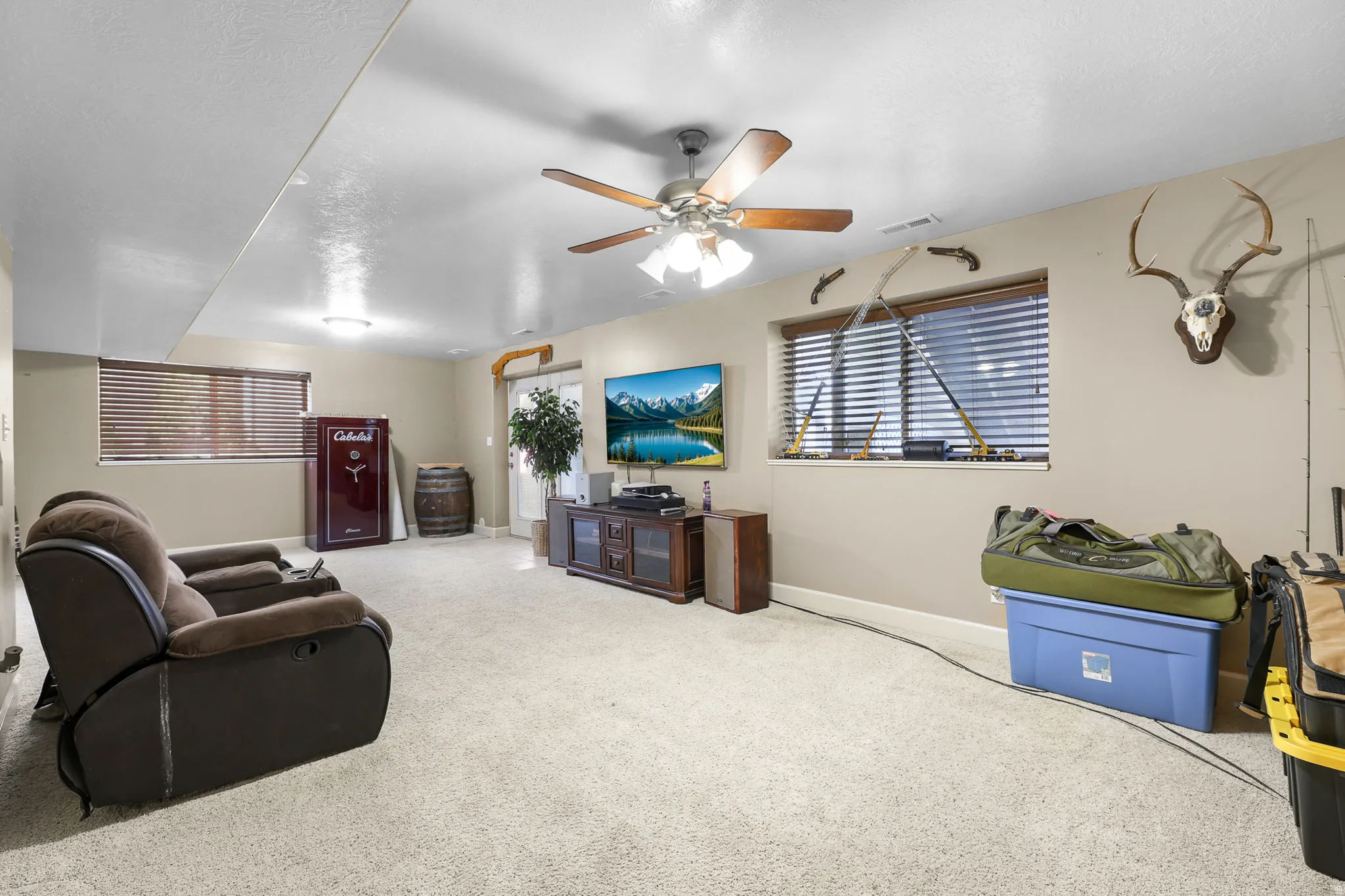 Spacious carpeted room featuring a ceiling fan, recessed lighting, two windows with blinds, and a built-in media console