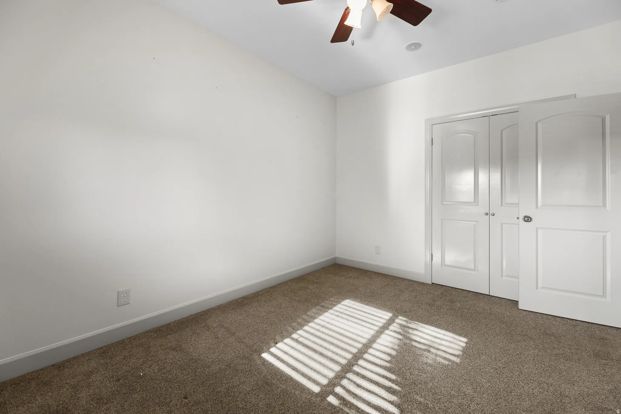 Carpeted room featuring white walls, a white trim, and a ceiling fan with light fixture