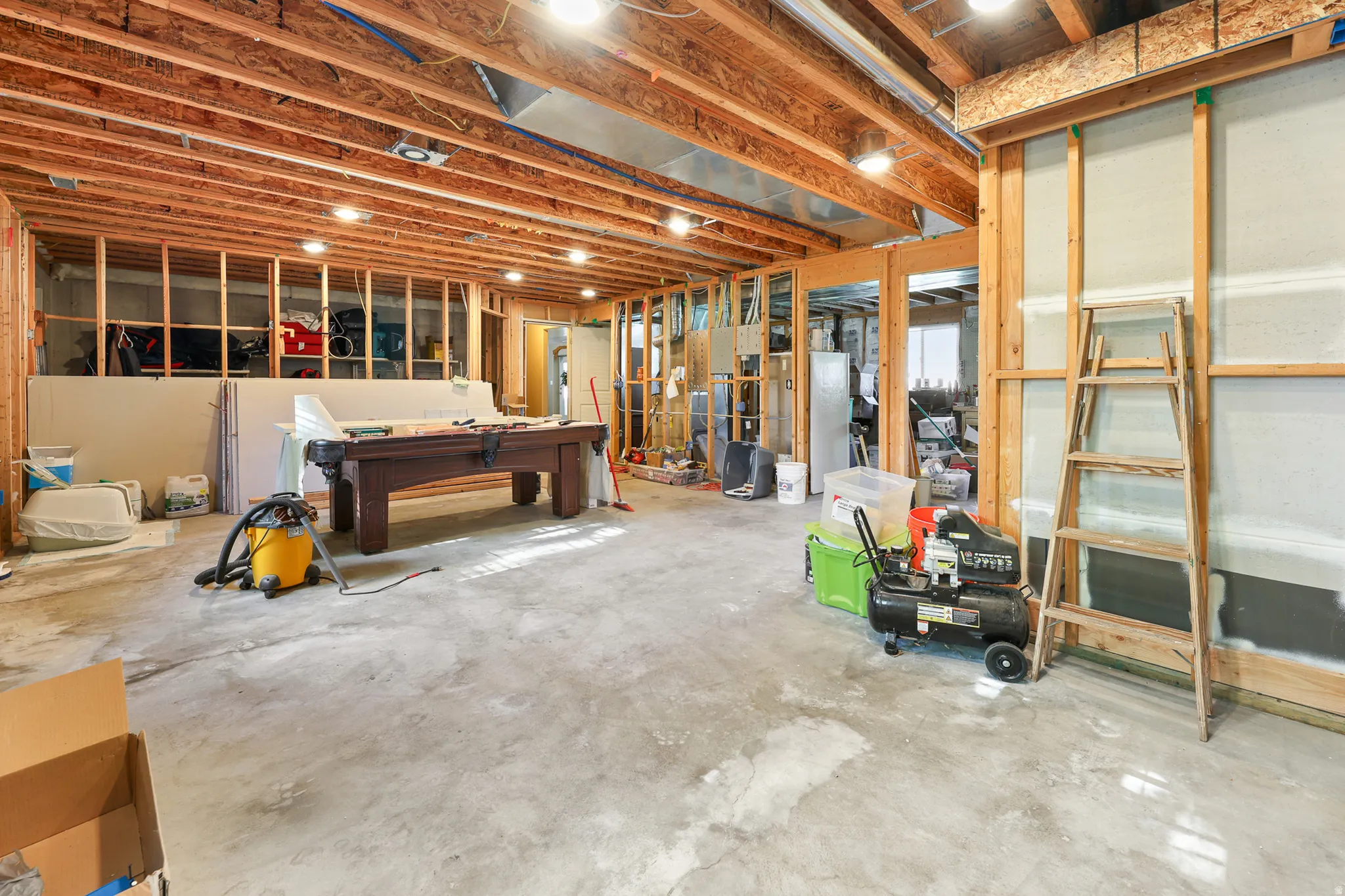 Unfinished basement area featuring exposed wood framing, concrete flooring, recessed lighting, and visible ceiling joists