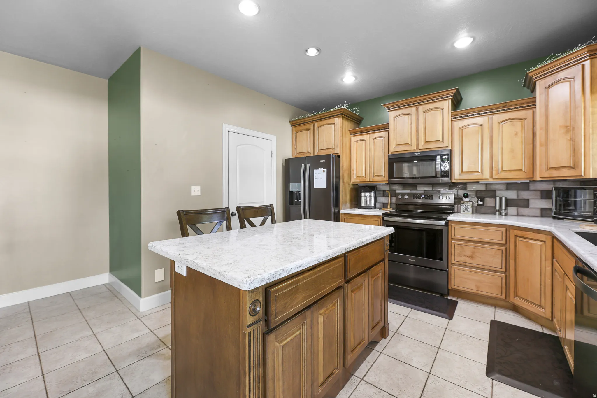 Kitchen featuring a central island with a light-toned countertop, wood cabinetry, stainless steel appliances, tile flooring, and recessed lighting