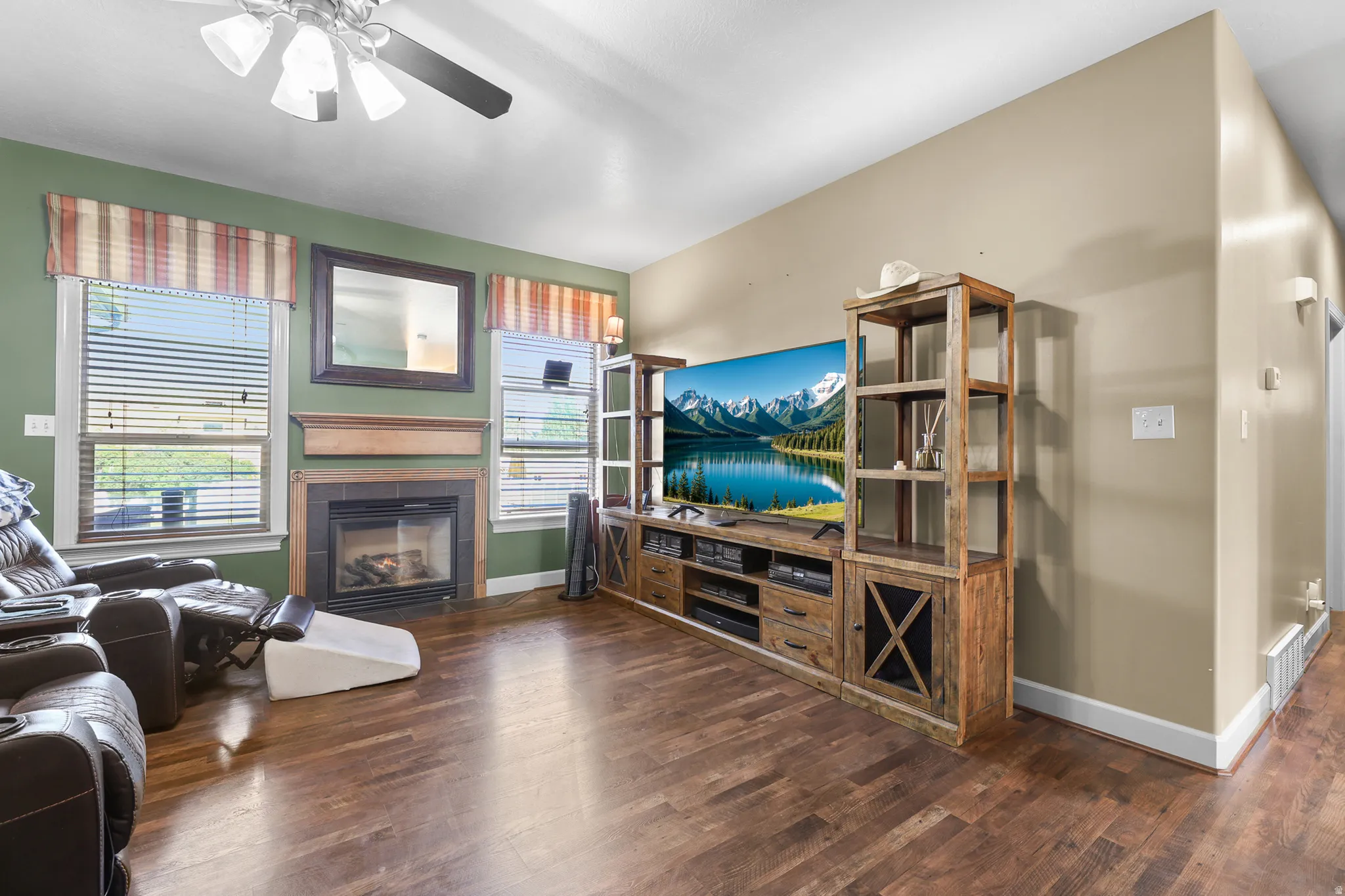 Spacious living area featuring wood-finish flooring, a fireplace with a wood mantle and dark tile surround, and multiple windows with blinds