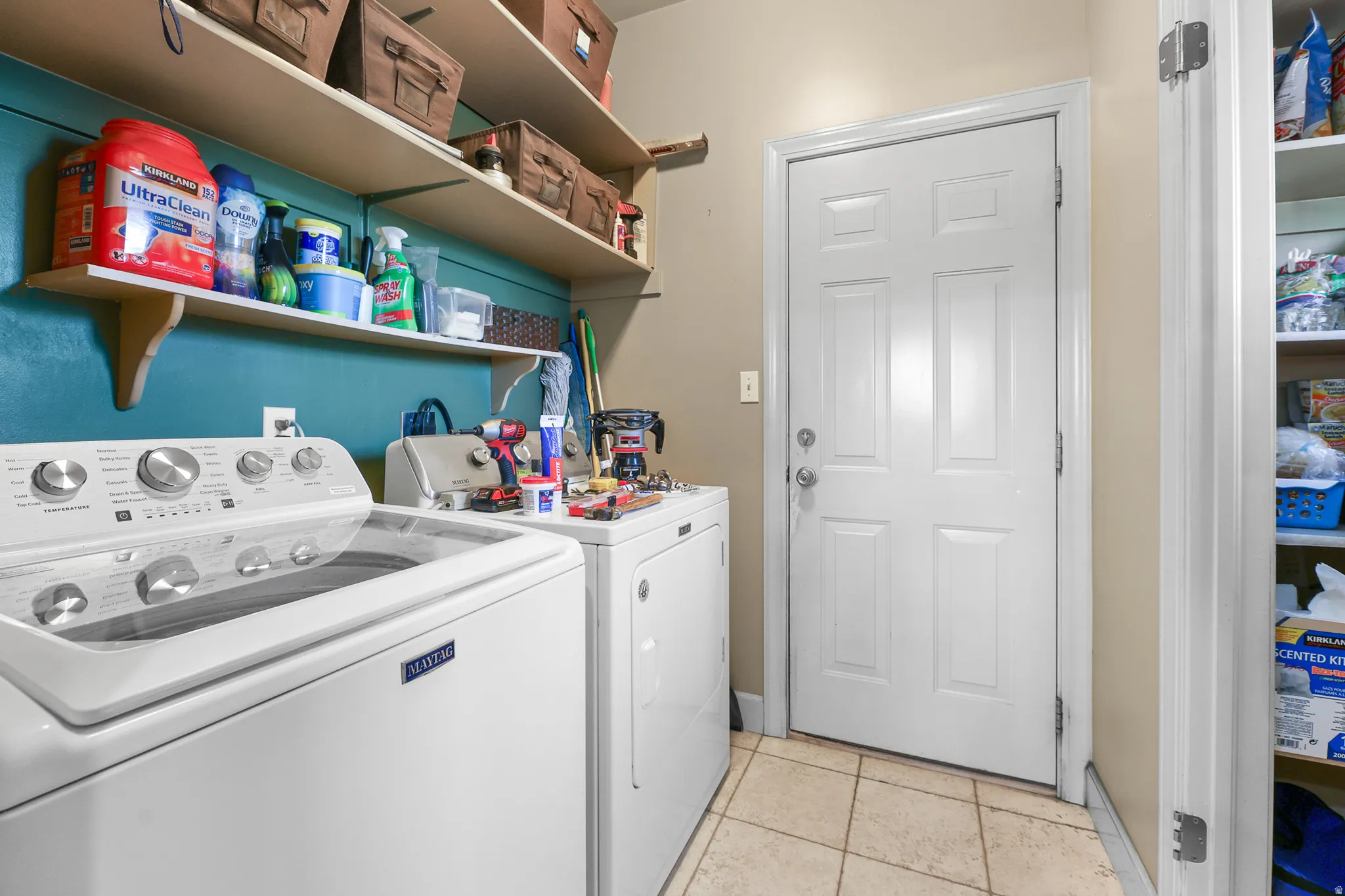 Dedicated utility space featuring a paneled door, light-toned tile flooring, and integrated shelving