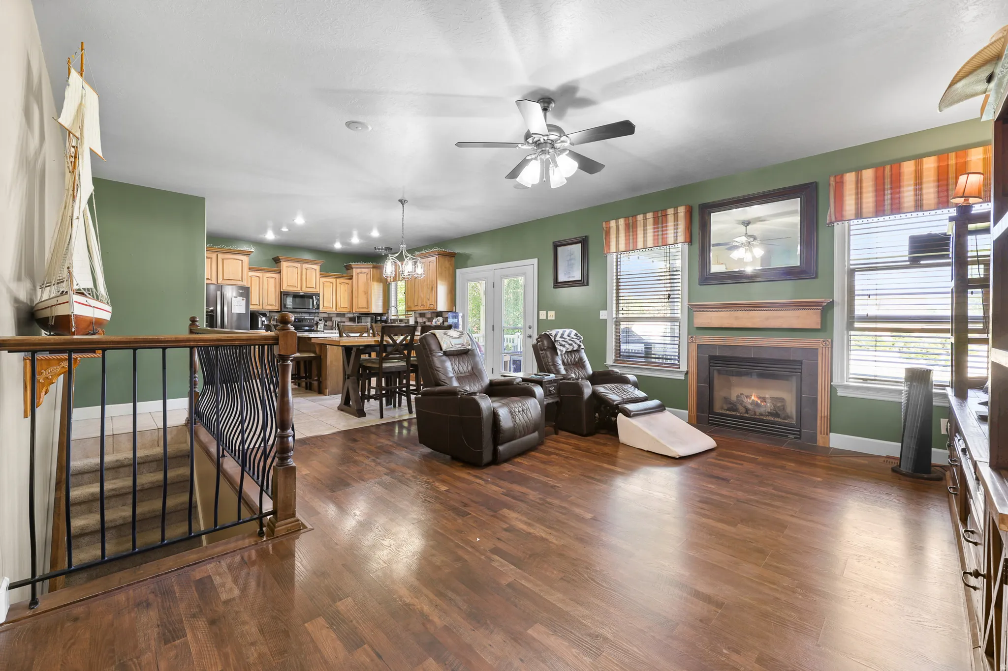 Open-concept living area featuring wood-finish flooring, a ceiling fan, and a fireplace with a wood mantle and tile surround
