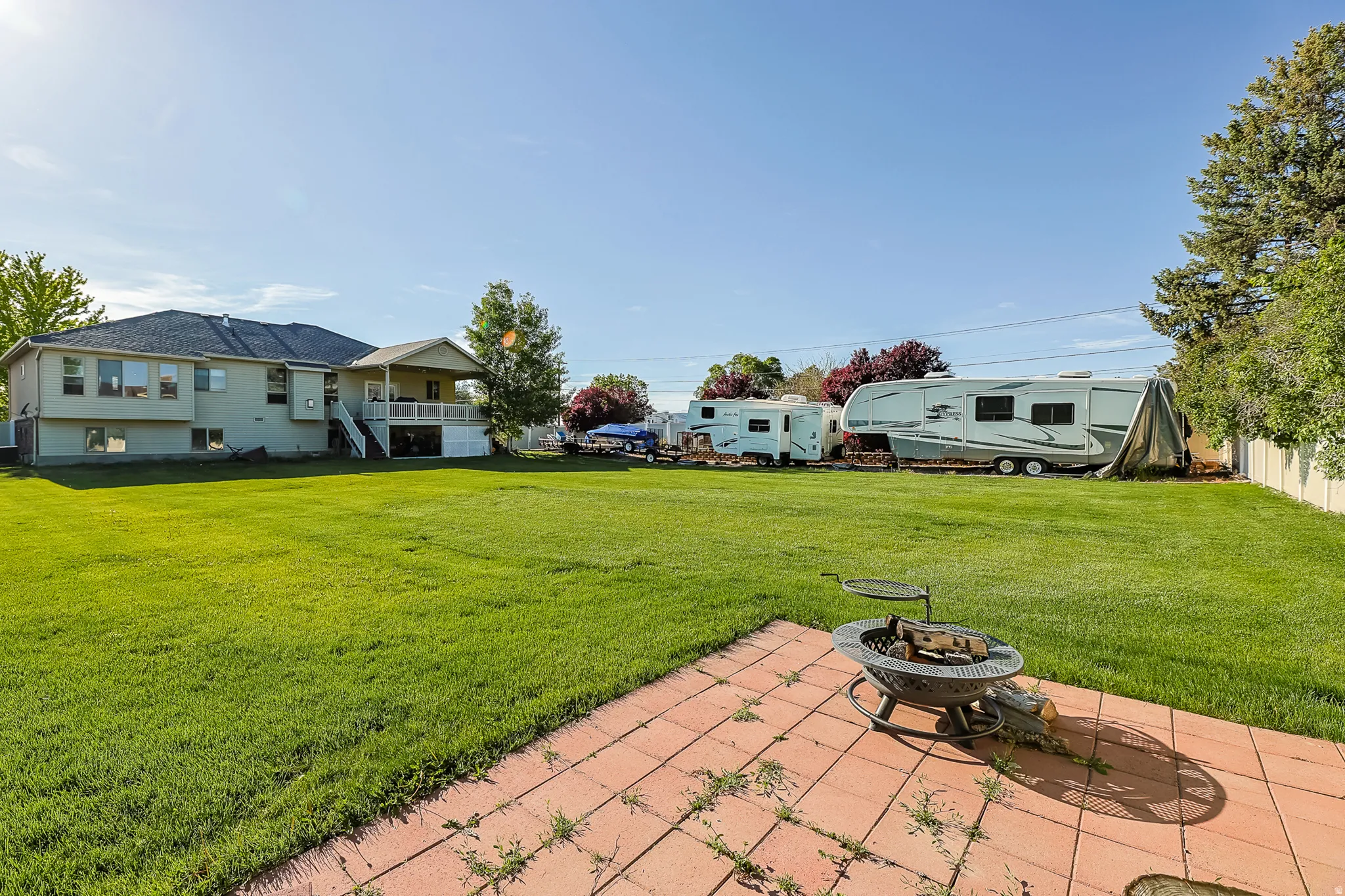 Expansive backyard featuring a large lawn area and a brick paver patio with a built-in fire pit