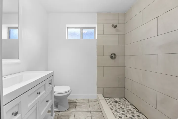 Shower with rectangular wall tiles and a hexagonal mosaic floor, white vanity with integrated sink, and a high-set window