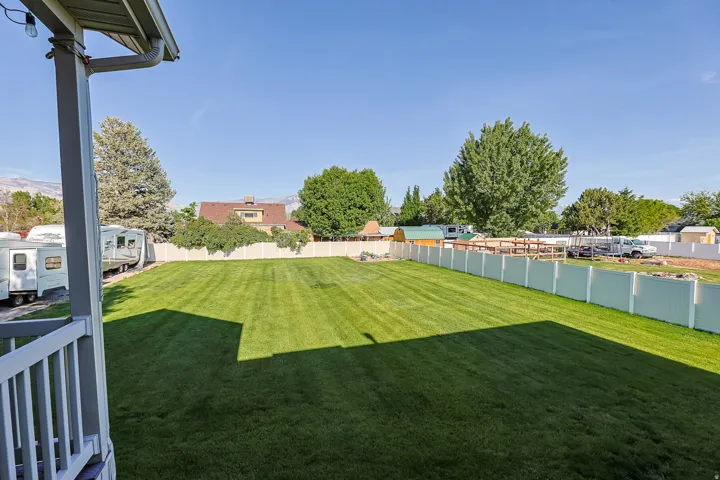 Expansive backyard featuring a manicured lawn, a full white privacy fence, and a partially visible porch with white railings