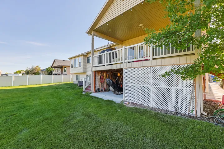 Expansive green lawn featuring a covered patio, upper-level deck, white lattice skirting, and a privacy fence