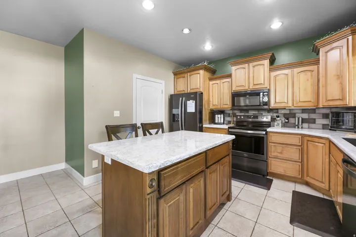 Kitchen featuring a central island with a light-toned countertop, wood cabinetry, stainless steel appliances, tile flooring, and recessed lighting