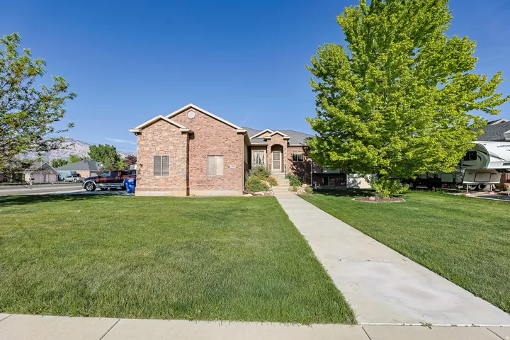 Brick exterior with multiple gables, a concrete walkway, and a landscaped front yard with mature trees