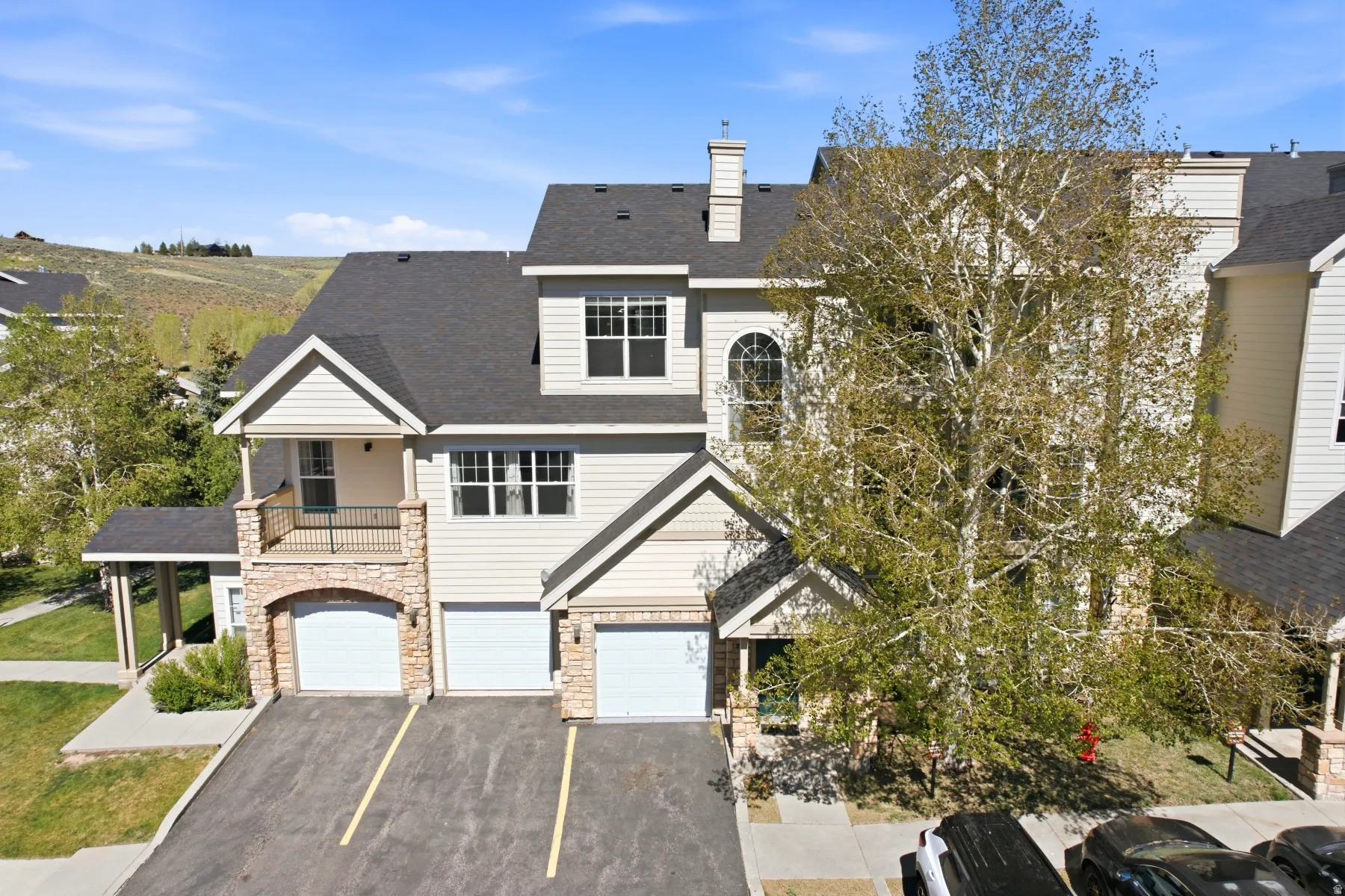 Multi-level townhome featuring stone accents, light-colored siding, multiple balconies, a two-car garage, and a steeply pitched roof