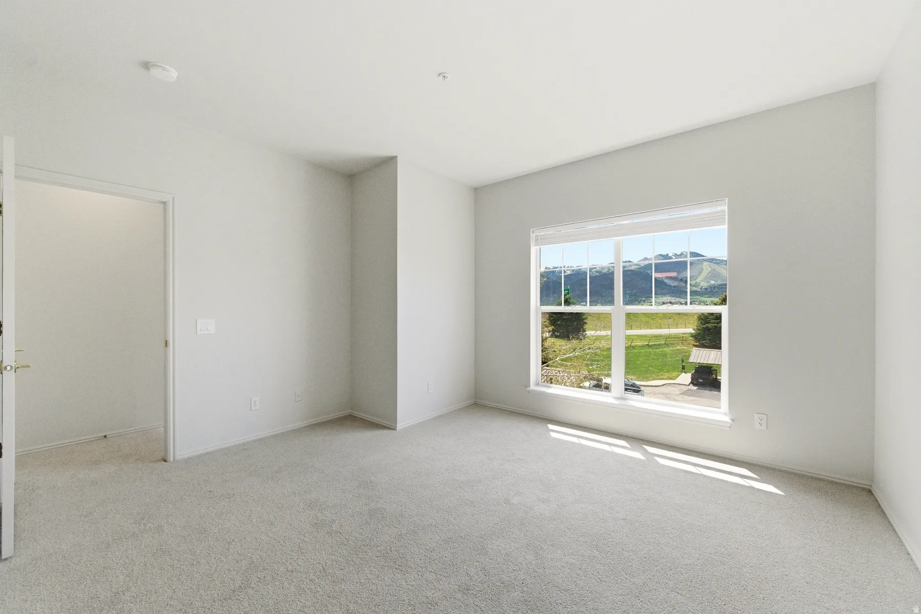 Spacious room featuring neutral carpeting, light-toned walls, and a large window with a mountain backdrop