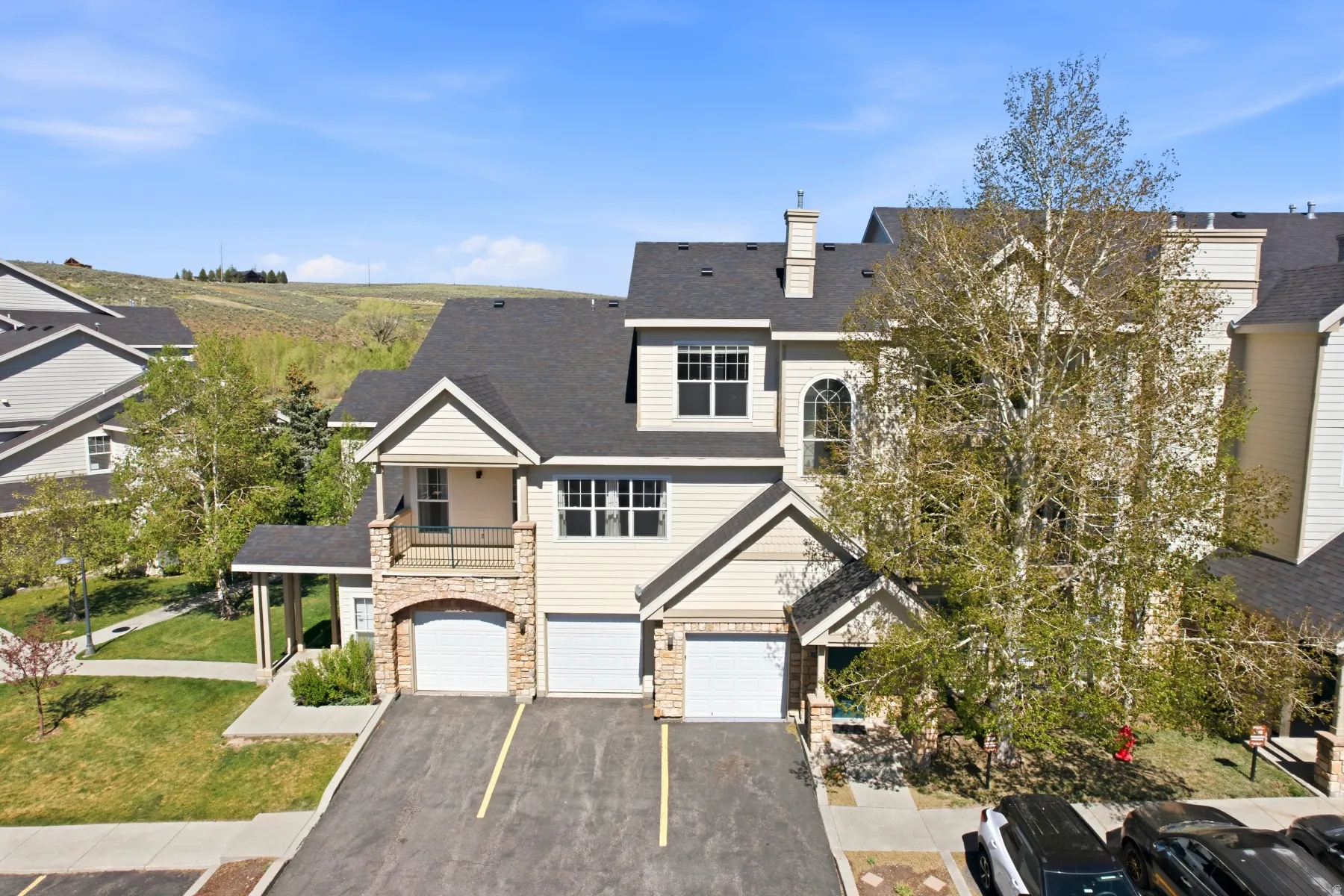Multi-level townhome featuring a stone and siding exterior, multiple garage bays, and an upper-level balcony with a metal railing