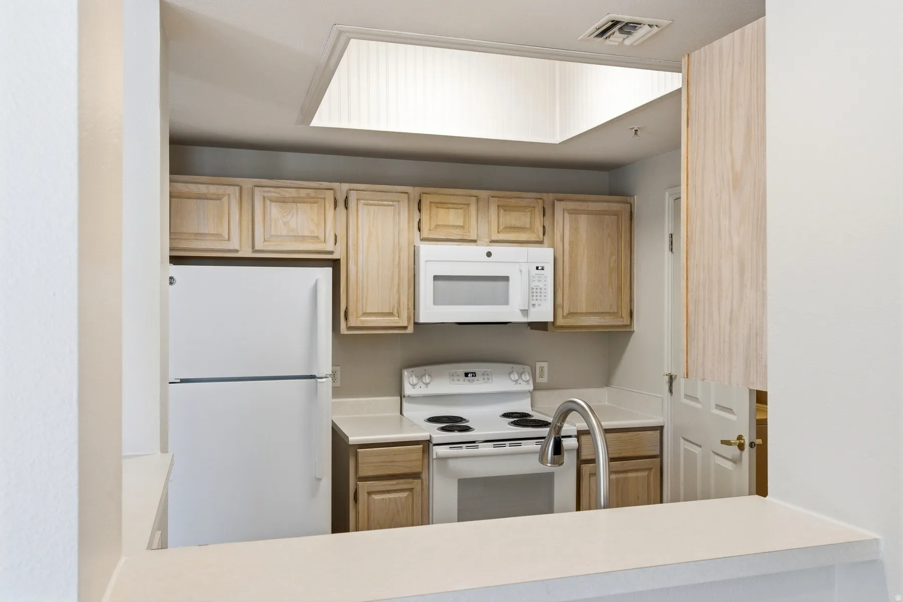 Kitchen featuring light wood cabinetry, white appliances, a contemporary pull-down faucet, solid surface countertops, and a ceiling light panel
