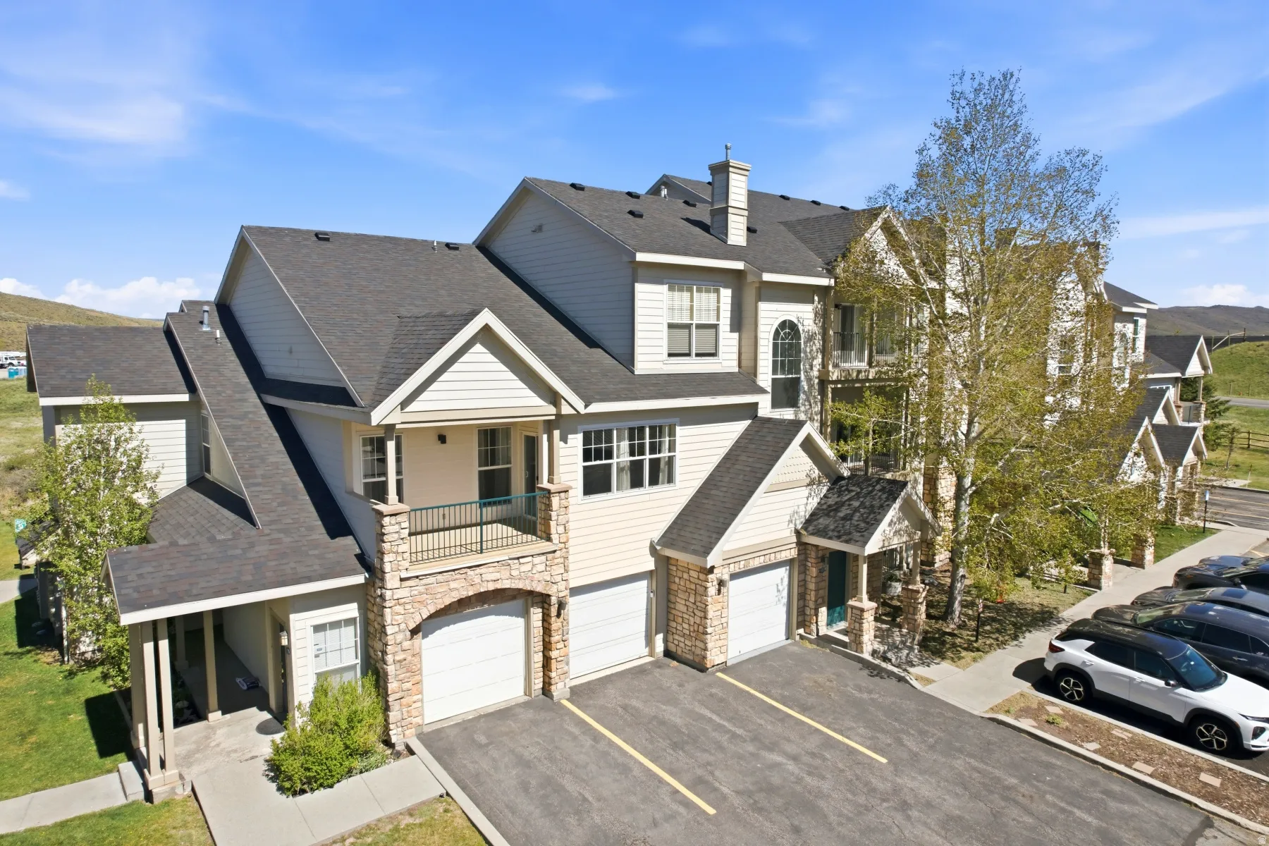 Multi-story townhome building featuring light-toned siding, dark shingled roofs, and stone accents