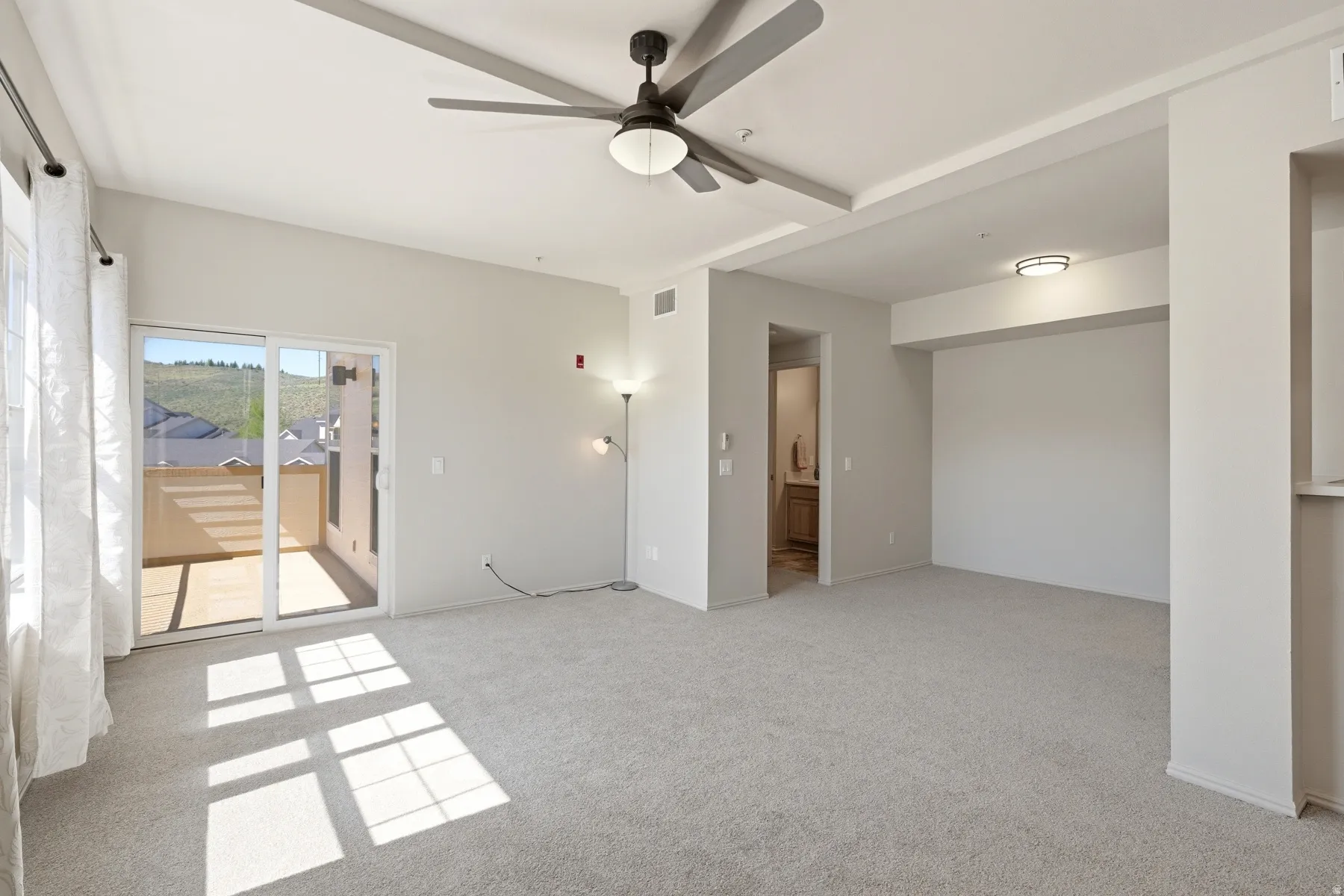 Spacious carpeted interior featuring a ceiling fan, sliding glass doors to a private balcony, and recessed lighting