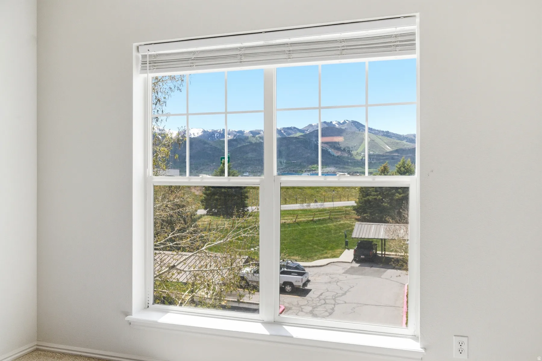 Large window with white frame and grids, offering a broad scenic backdrop of snow-capped mountains and green hills
