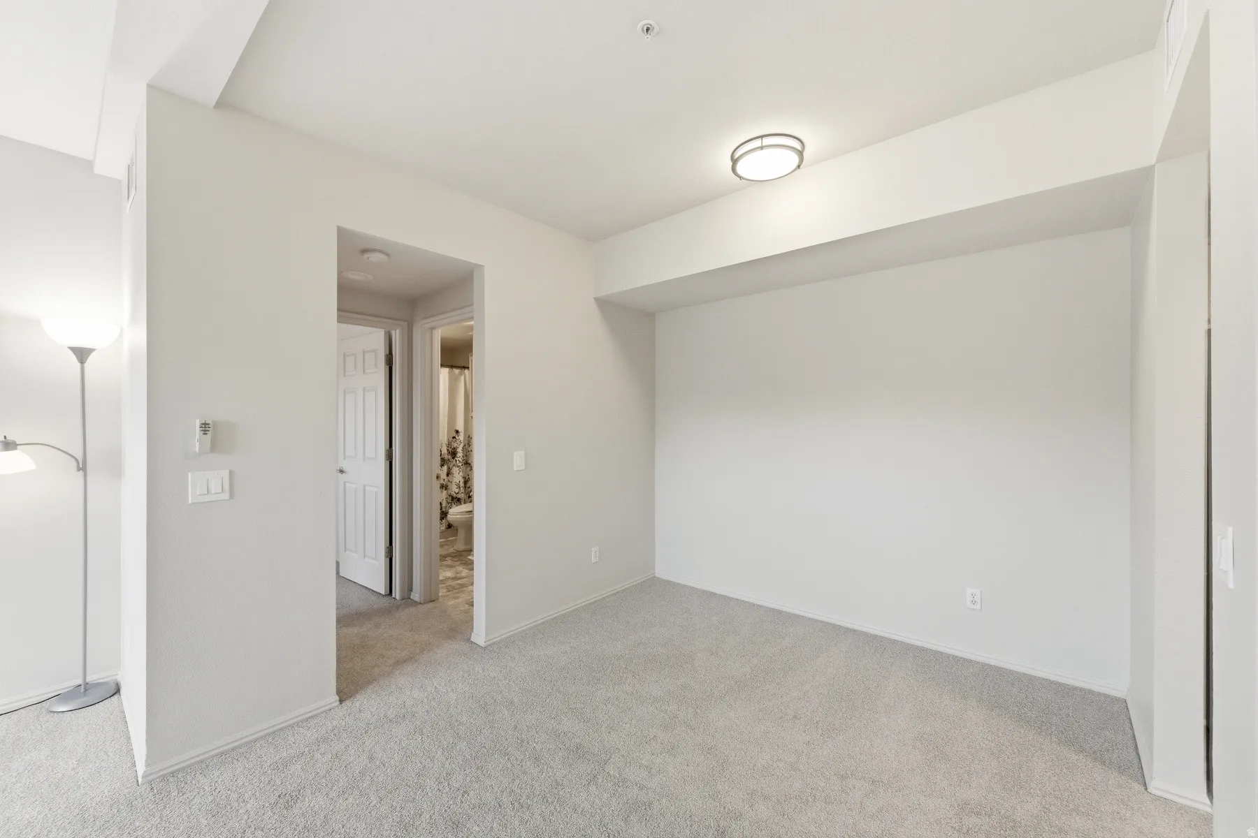 Carpeted interior space featuring a flush-mount ceiling light fixture, neutral wall finishes, and a doorway leading to an additional interior room